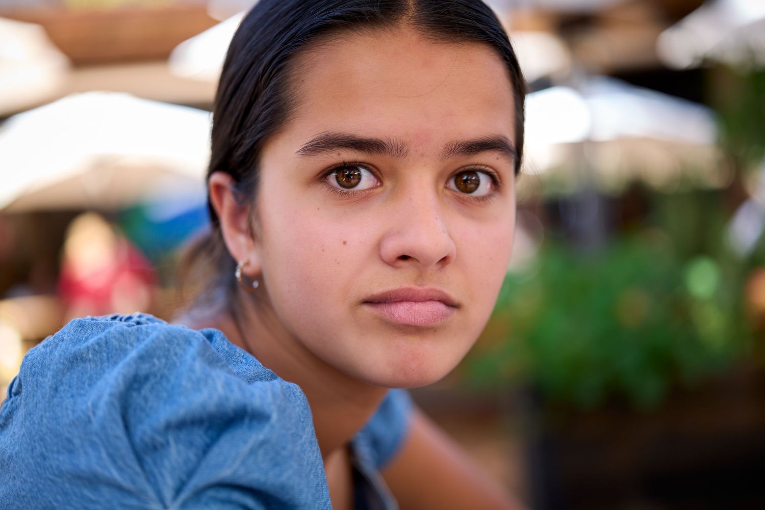 Person in denim jacket looks thoughtfully into the distance in an outdoor setting.