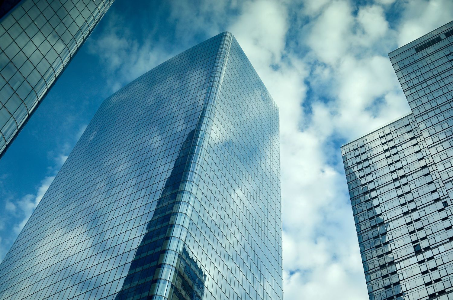 Modern glass skyscrapers reflecting blue sky and white clouds in an urban setting.