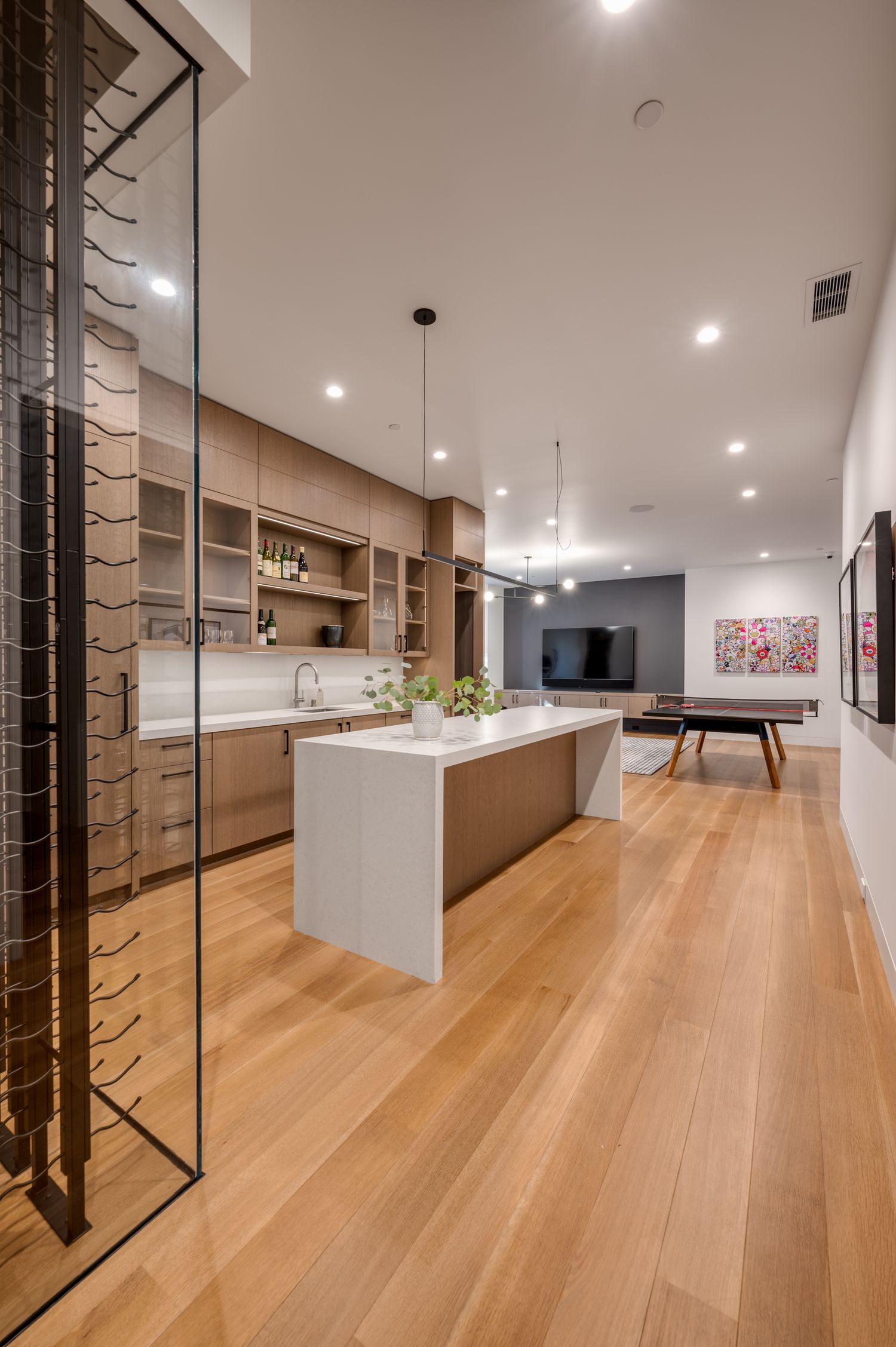 Modern open-concept kitchen and living space with wood floors and white waterfall island counter.