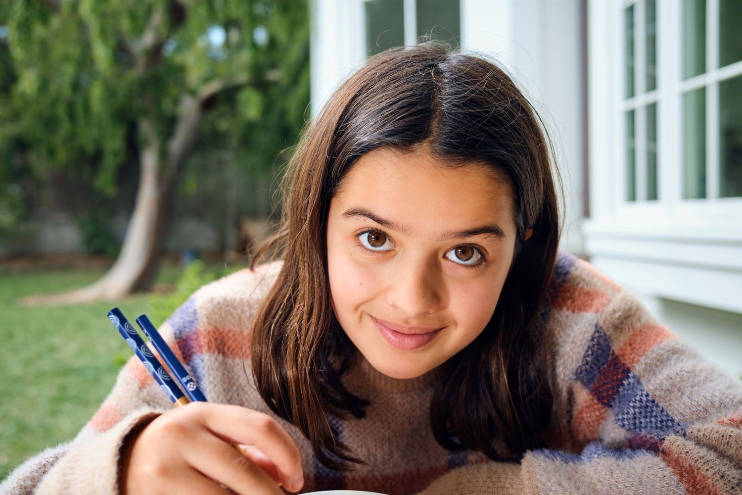 A person in a plaid sweater writes with a blue pen while studying.