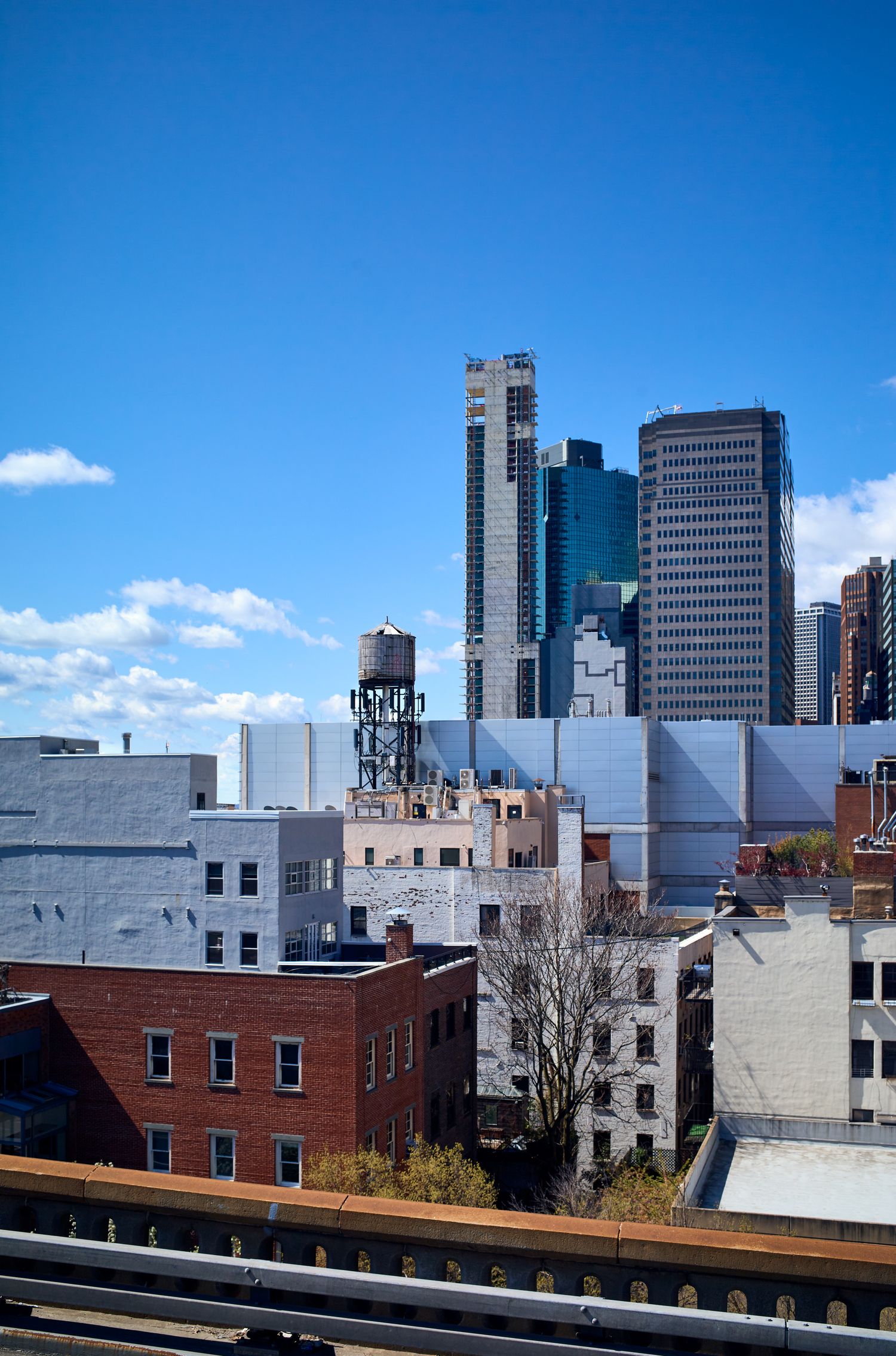 Modern skyscrapers and brick buildings create an urban skyline against a bright blue sky in a city setting.
