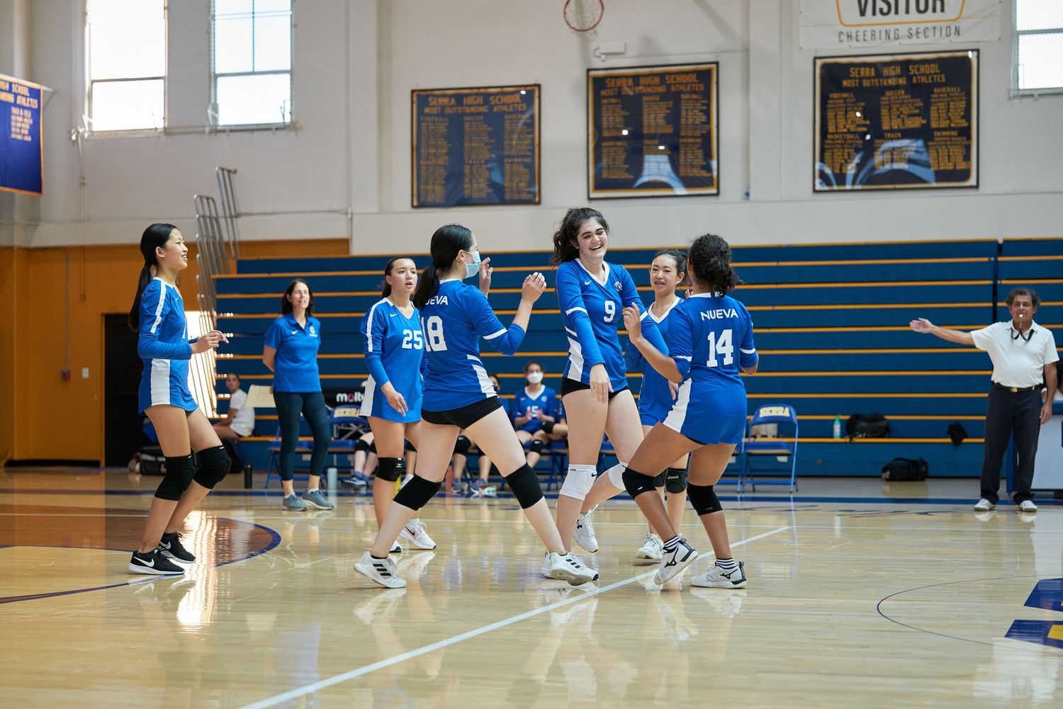 Team of volleyball players in blue uniforms celebrating during indoor match.