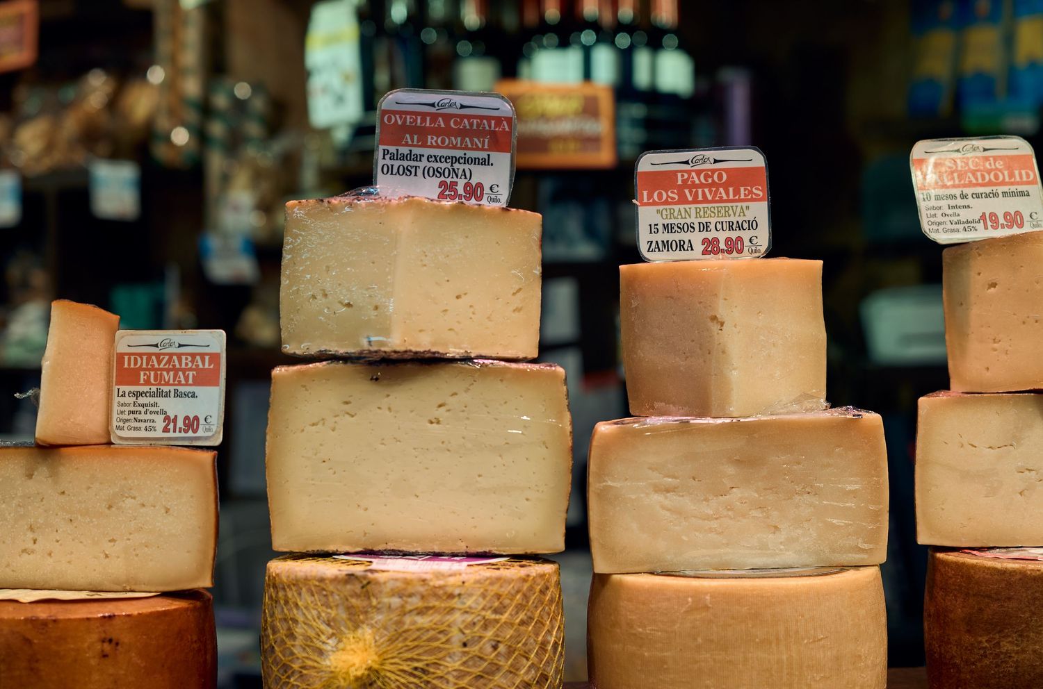 Large wheels of aged cheese stacked with price tags in a delicatessen display.