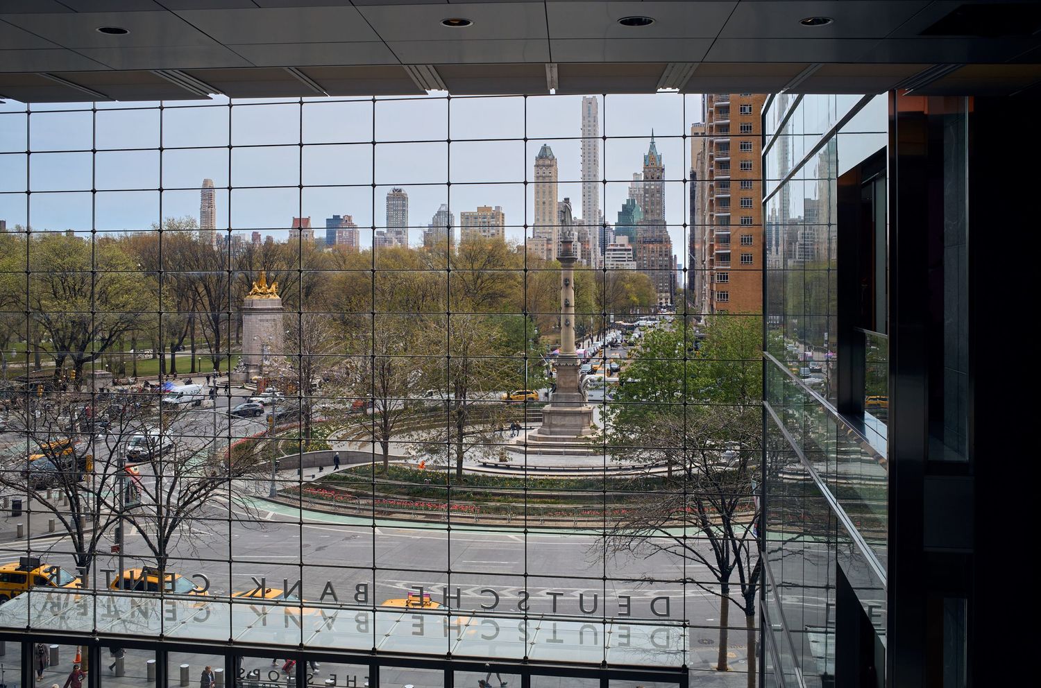 City skyline view through glass windows with trees and urban infrastructure in the foreground.