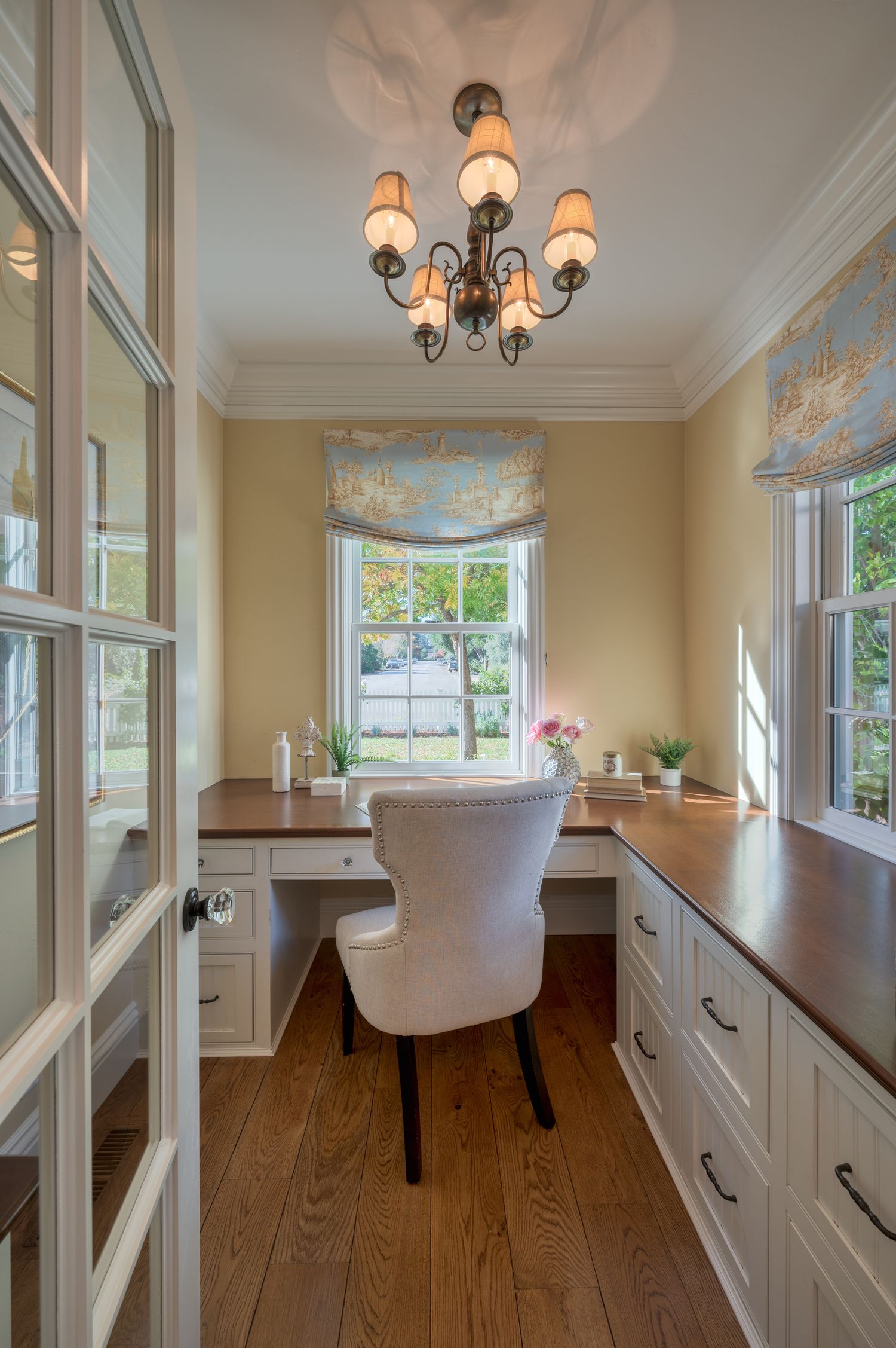 Cozy home office nook with built-in desk, chandelier, and white cabinetry.