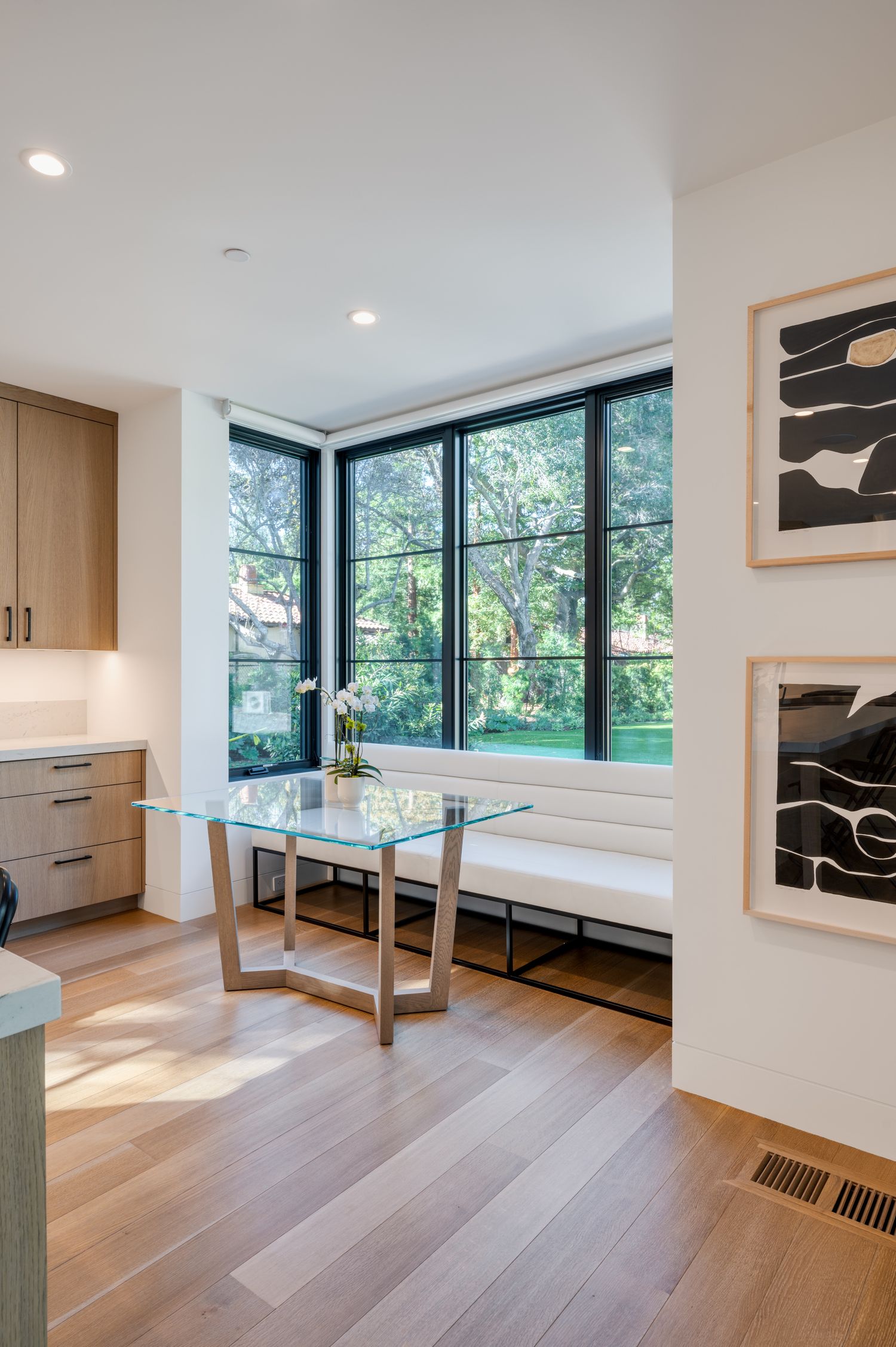 Bright breakfast nook with corner windows, modern glass table, and abstract wall art.