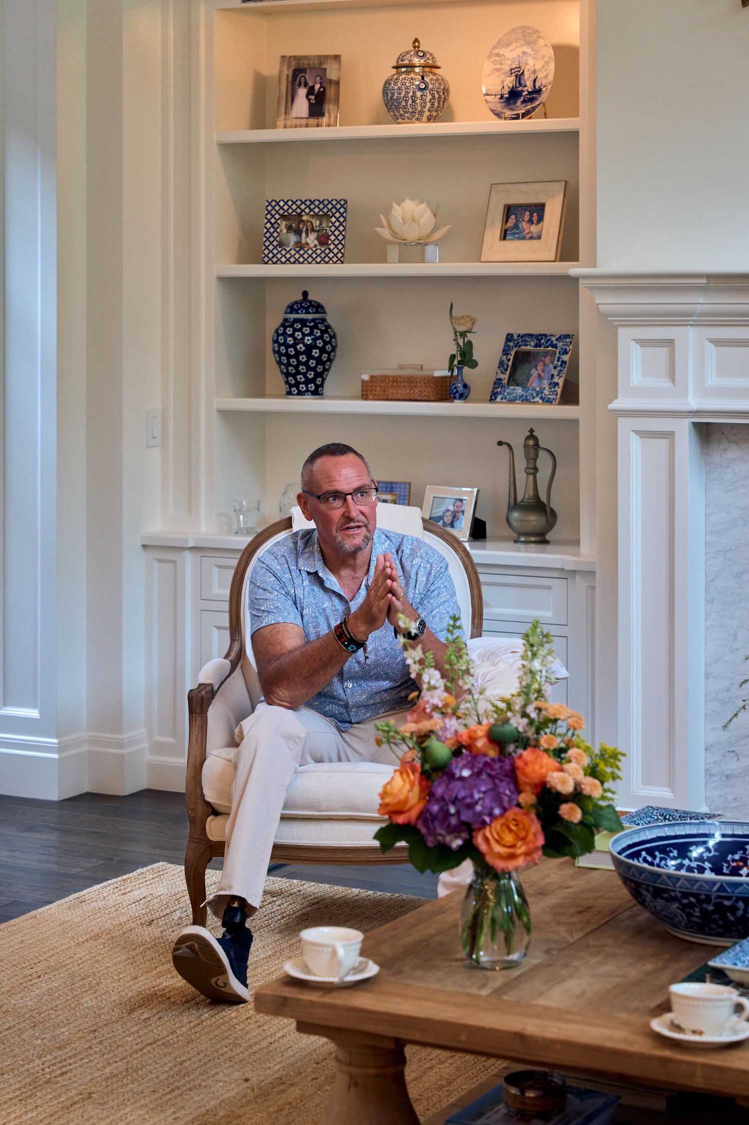 Person sitting in elegant living room with floral arrangement and built-in shelving.