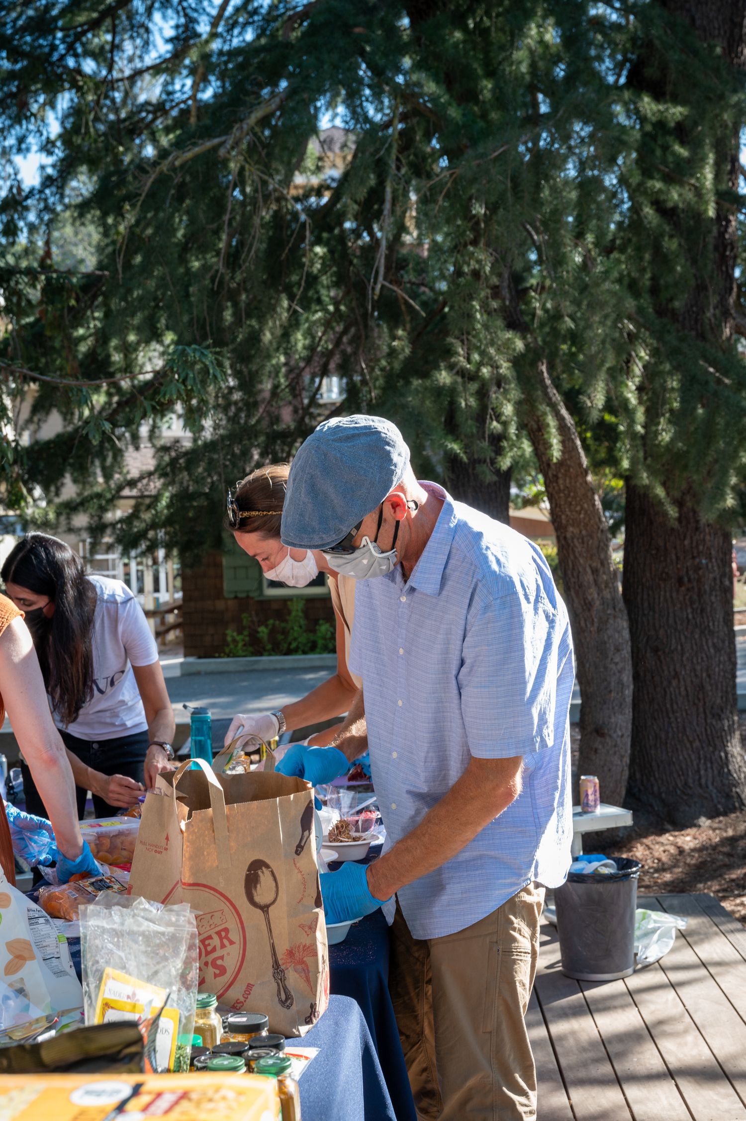 Person in mask and cap sorts through items at an outdoor table.