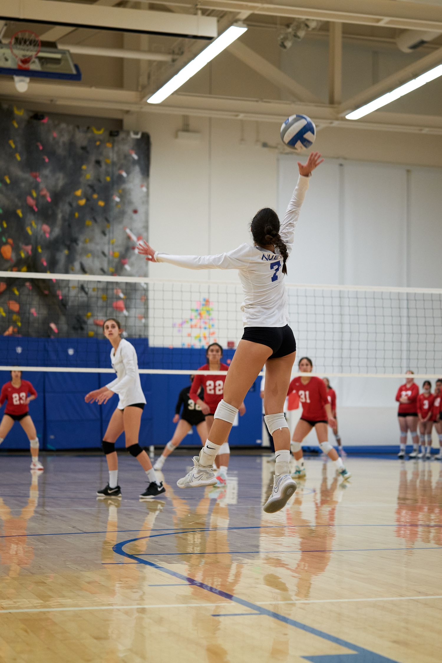 A volleyball player jumps high to serve the ball during an indoor match.