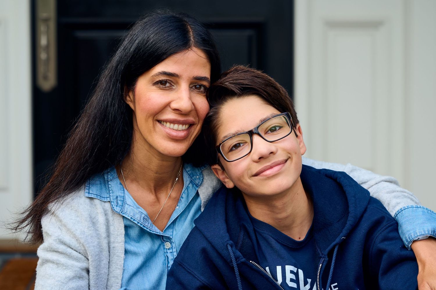 Two people in casual attire pose together on front porch steps.