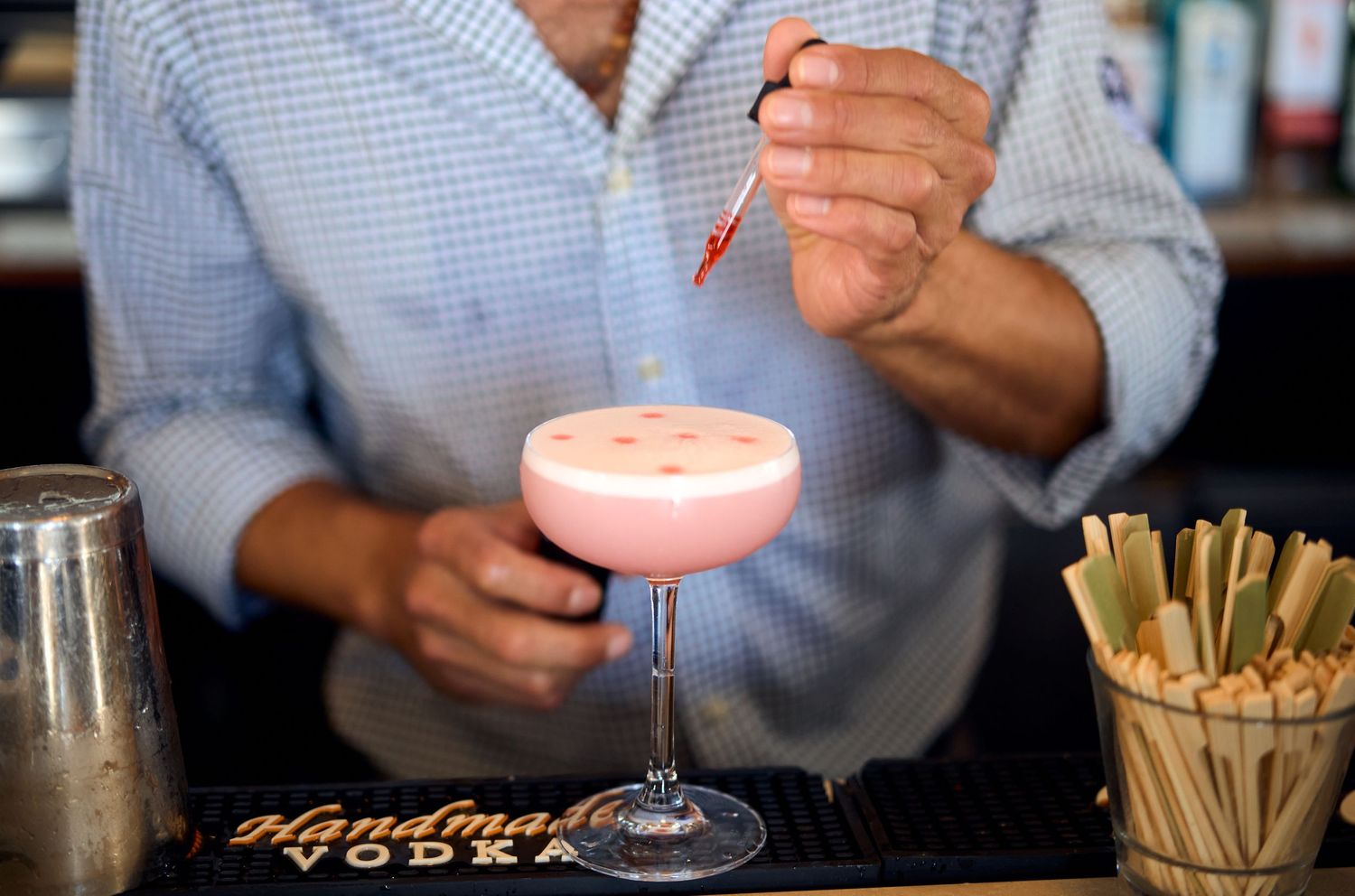 A pink cocktail being garnished by a bartender at an upscale bar.