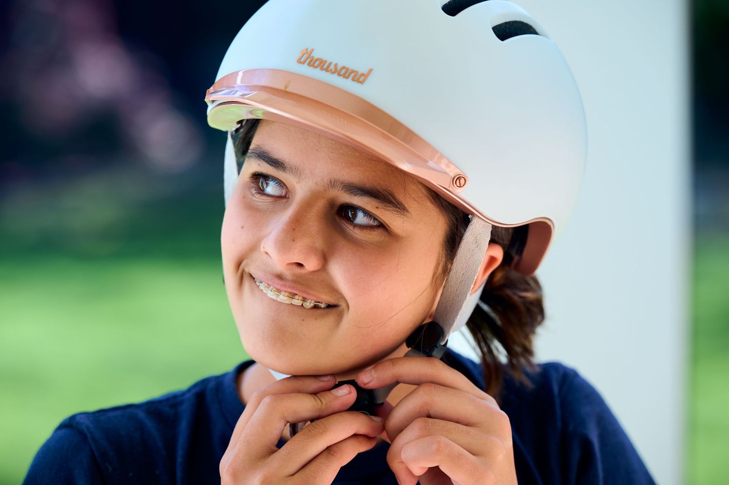 Person in navy blue clothing adjusts white safety helmet while smiling outdoors.