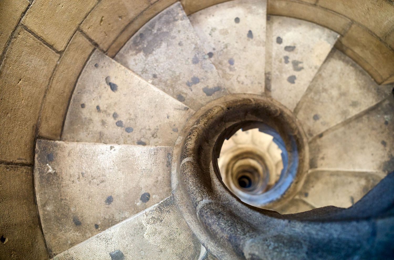 Spiral stone staircase viewed from above creating a mesmerizing circular pattern with natural light.