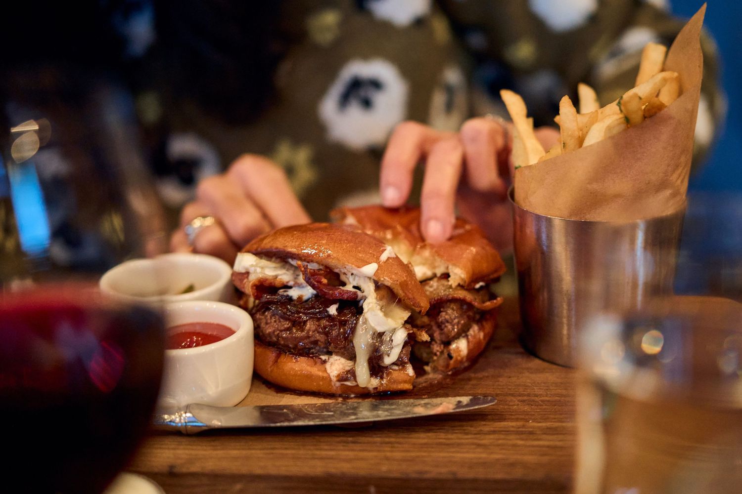 Juicy gourmet burger with french fries served on a wooden board with dipping sauce.