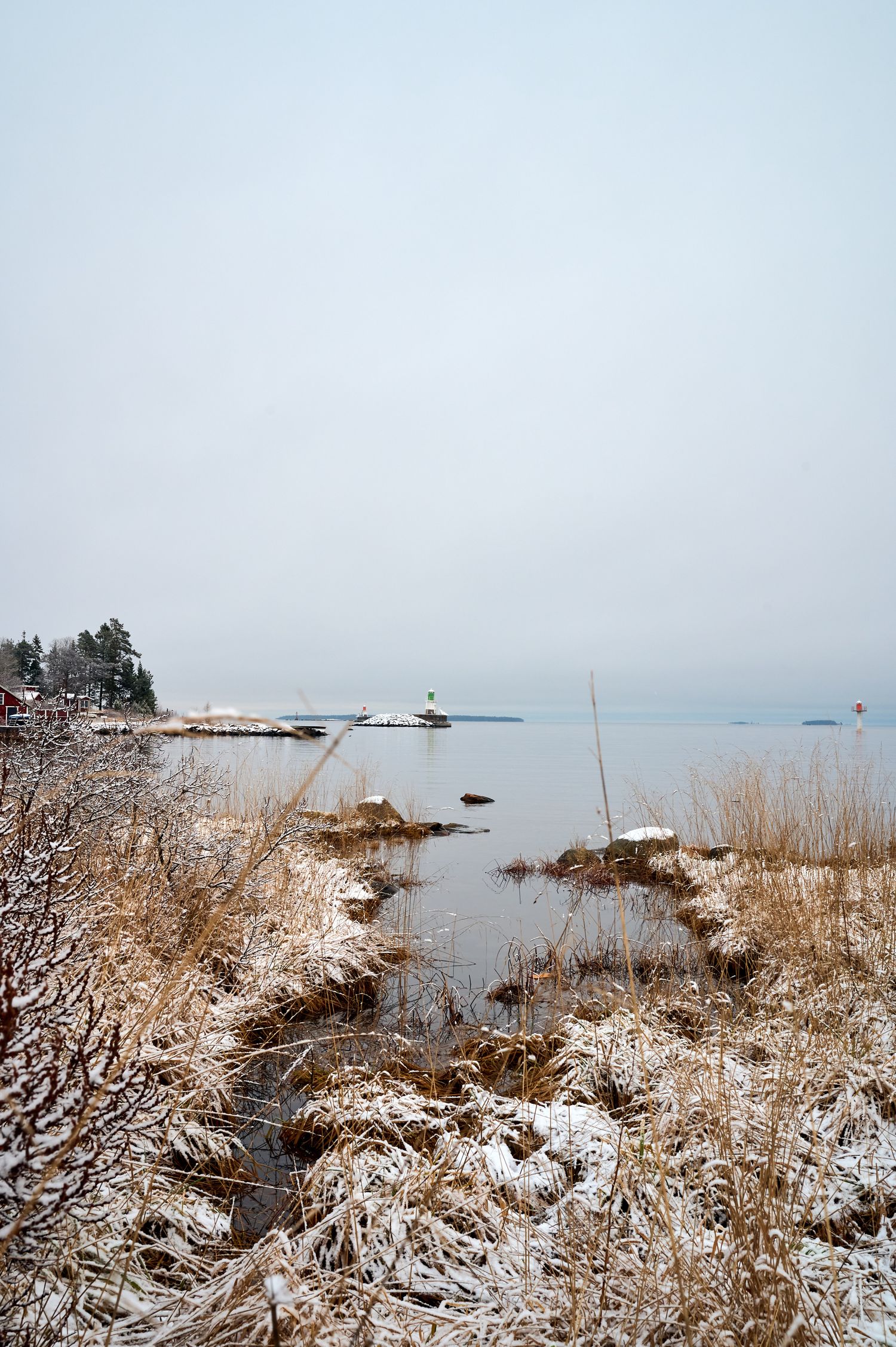 Snow-covered coastal landscape with lighthouse visible in distance across icy winter waters.