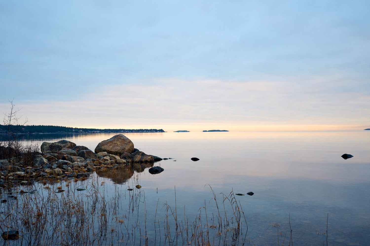 Tranquil lake landscape at sunset with rocky shoreline and calm reflective water.