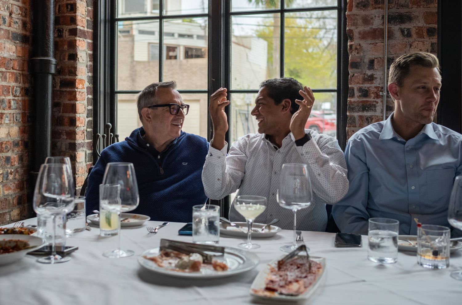 Three people dining at an elegant restaurant with wine glasses and plates on the table.