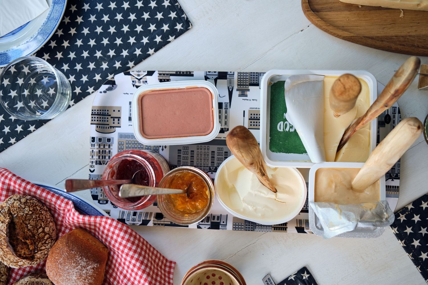 Overhead view of various sauces and condiments in bowls with wooden utensils on patterned tablecloth.