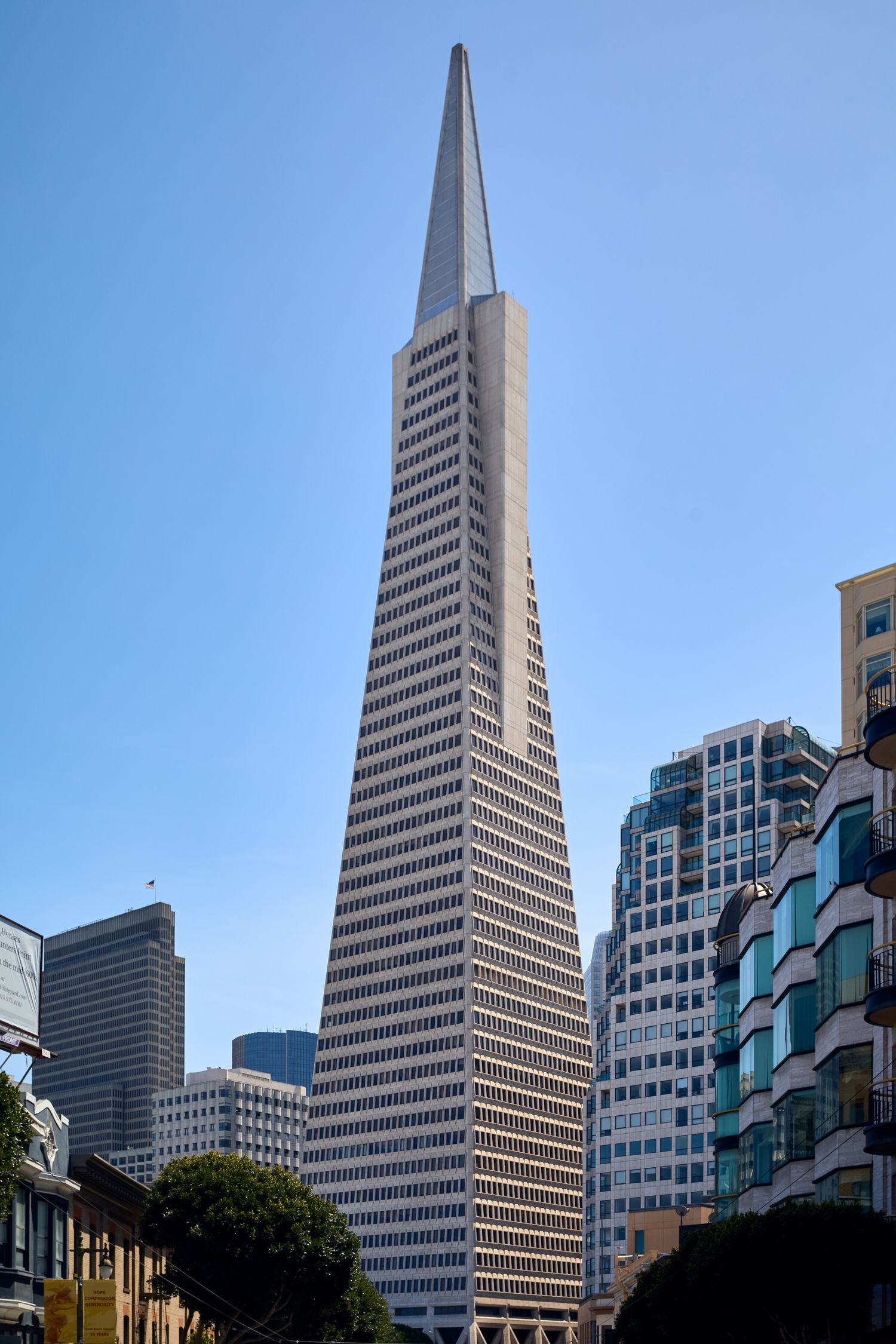 The Transamerica Pyramid building rises above other skyscrapers in downtown San Francisco against a bright blue sky.
