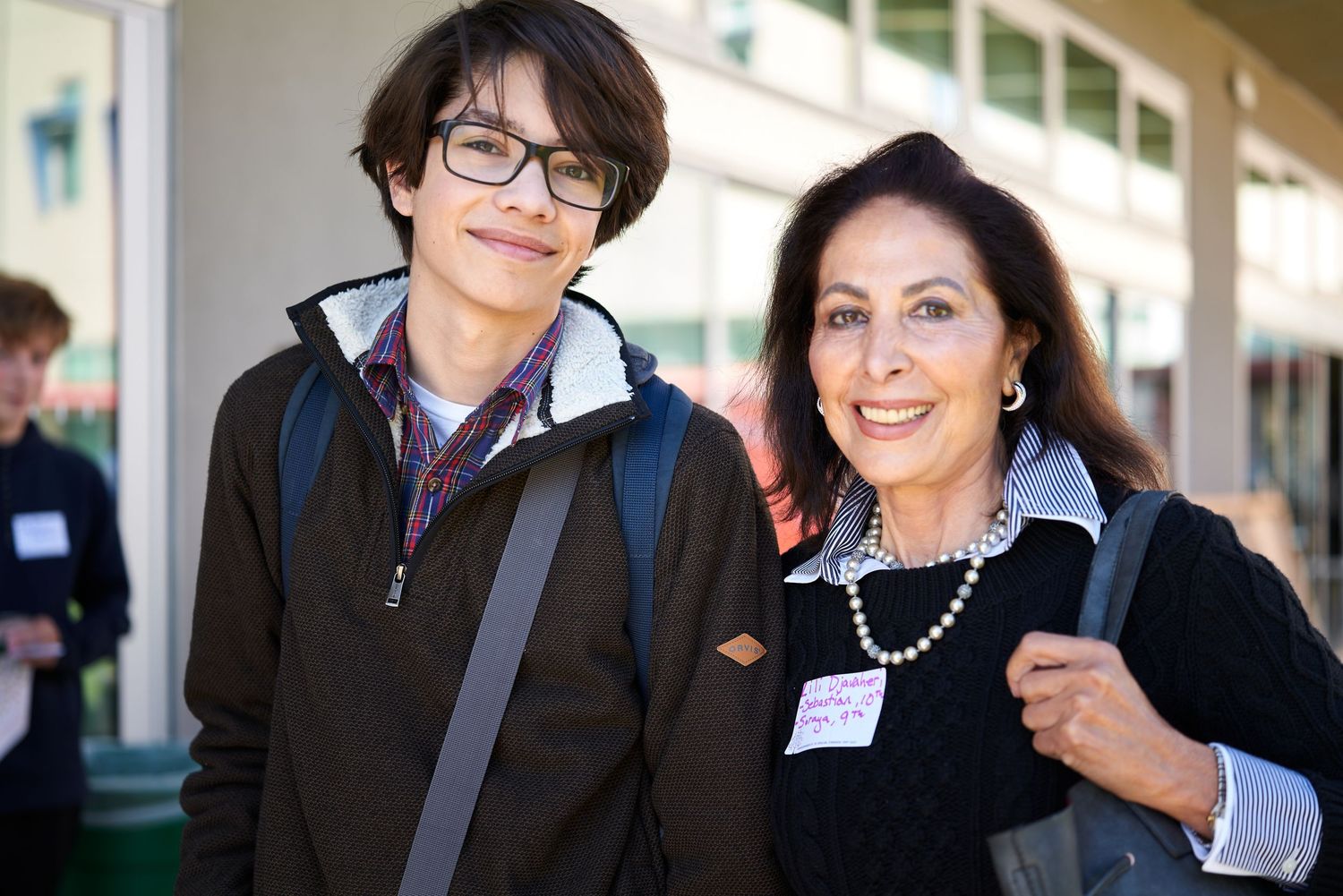 Student with backpack and advisor having friendly interaction outside educational building.