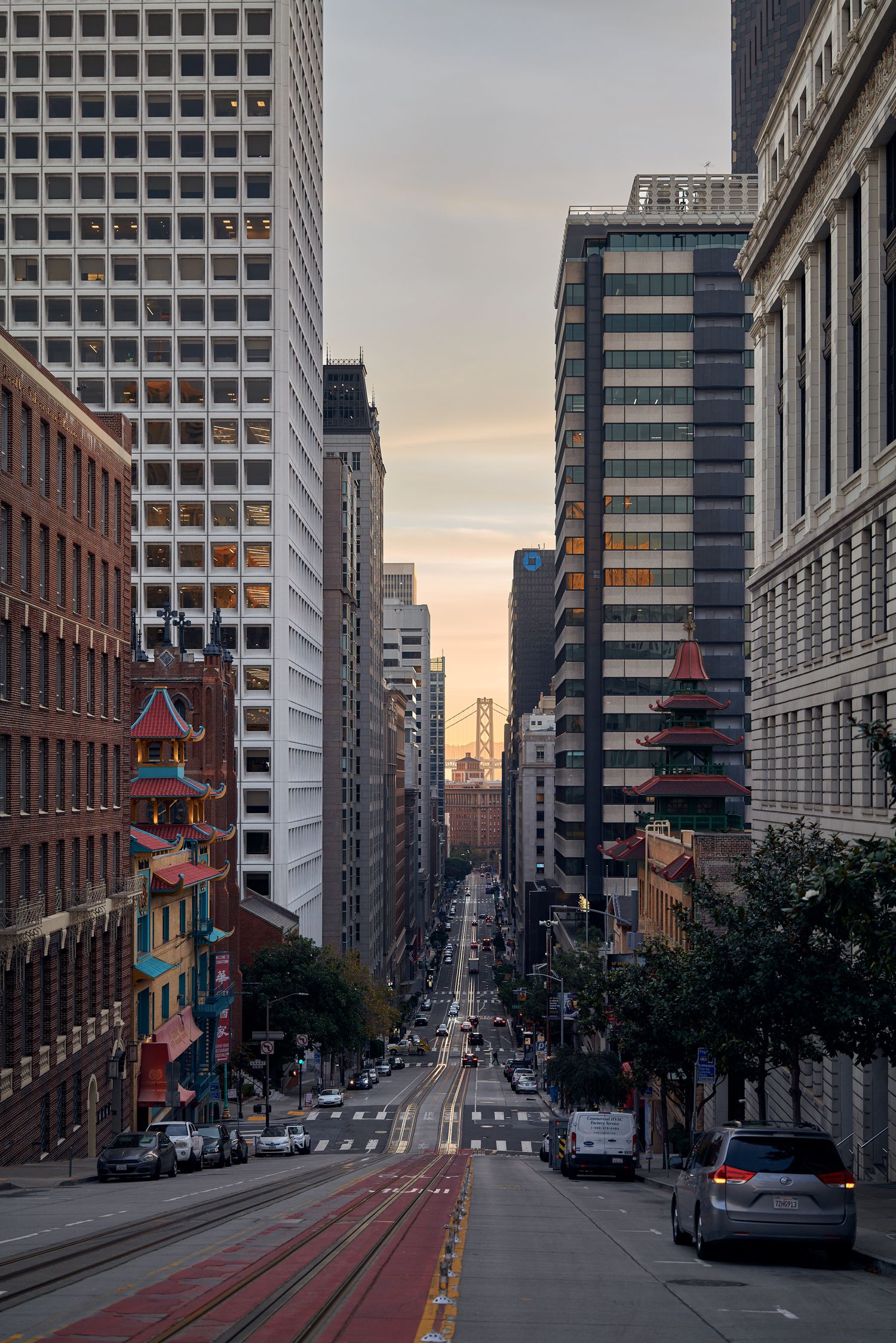 Urban canyon view down San Francisco street with tall buildings and transit lines at dusk.