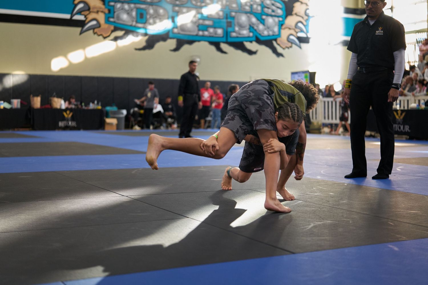 A martial artist executes a ground move during a competition on blue mats.
