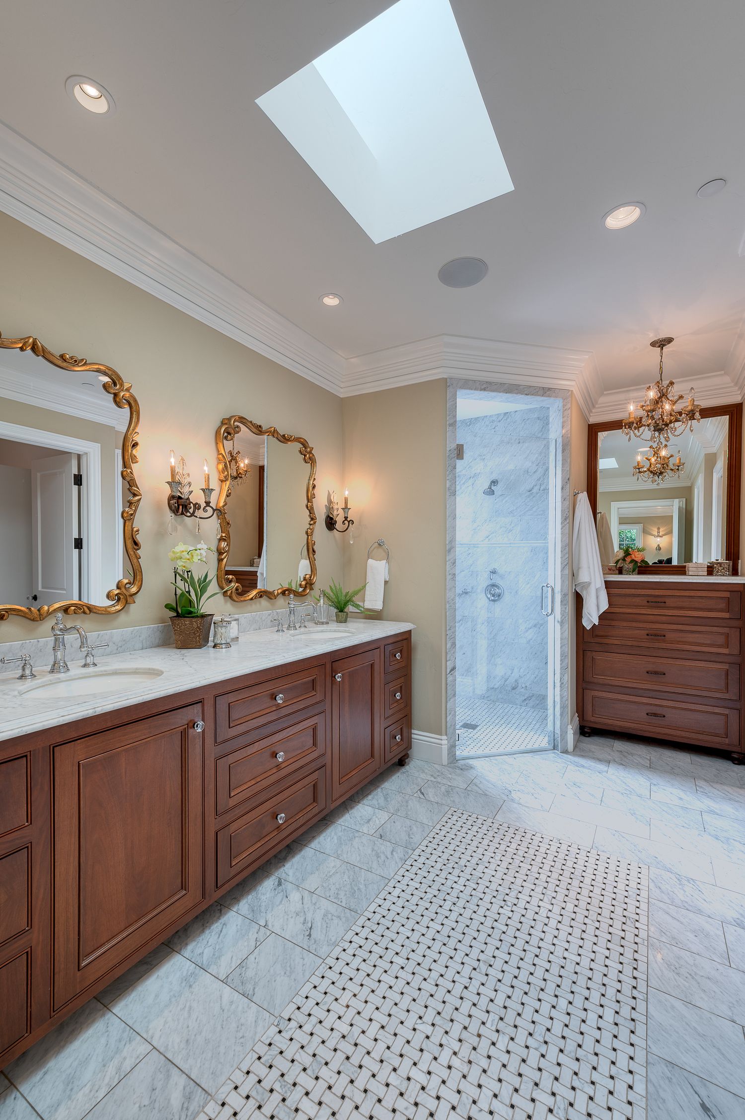 Luxurious marble bathroom with ornate gold mirrors, double vanity, and skylight overhead.