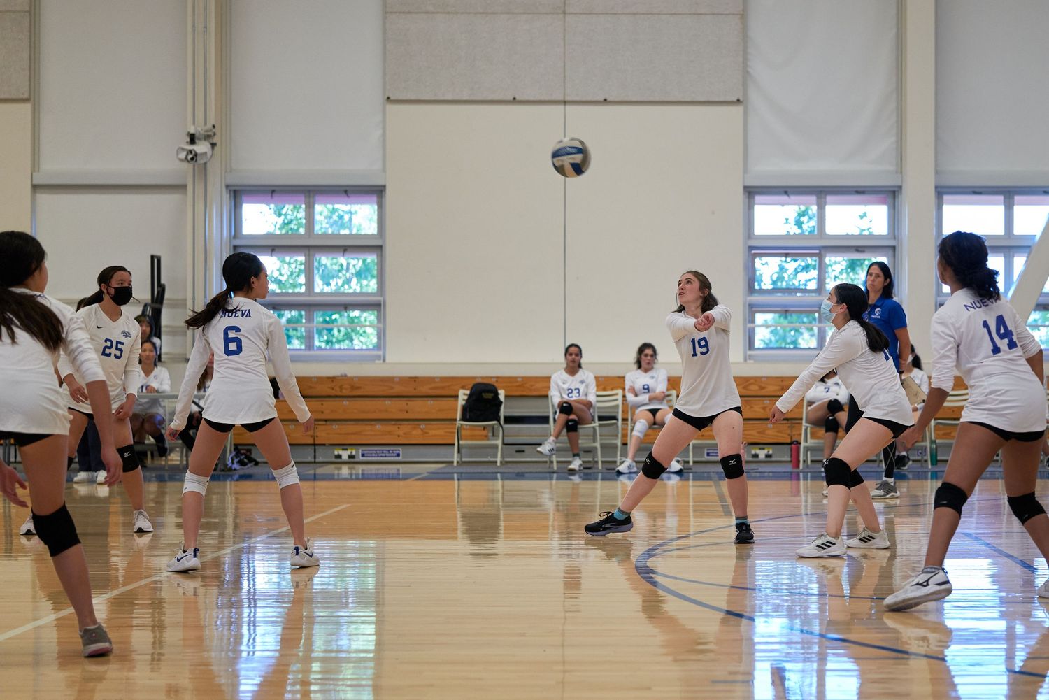 Volleyball players in white uniforms spread across court during indoor game.