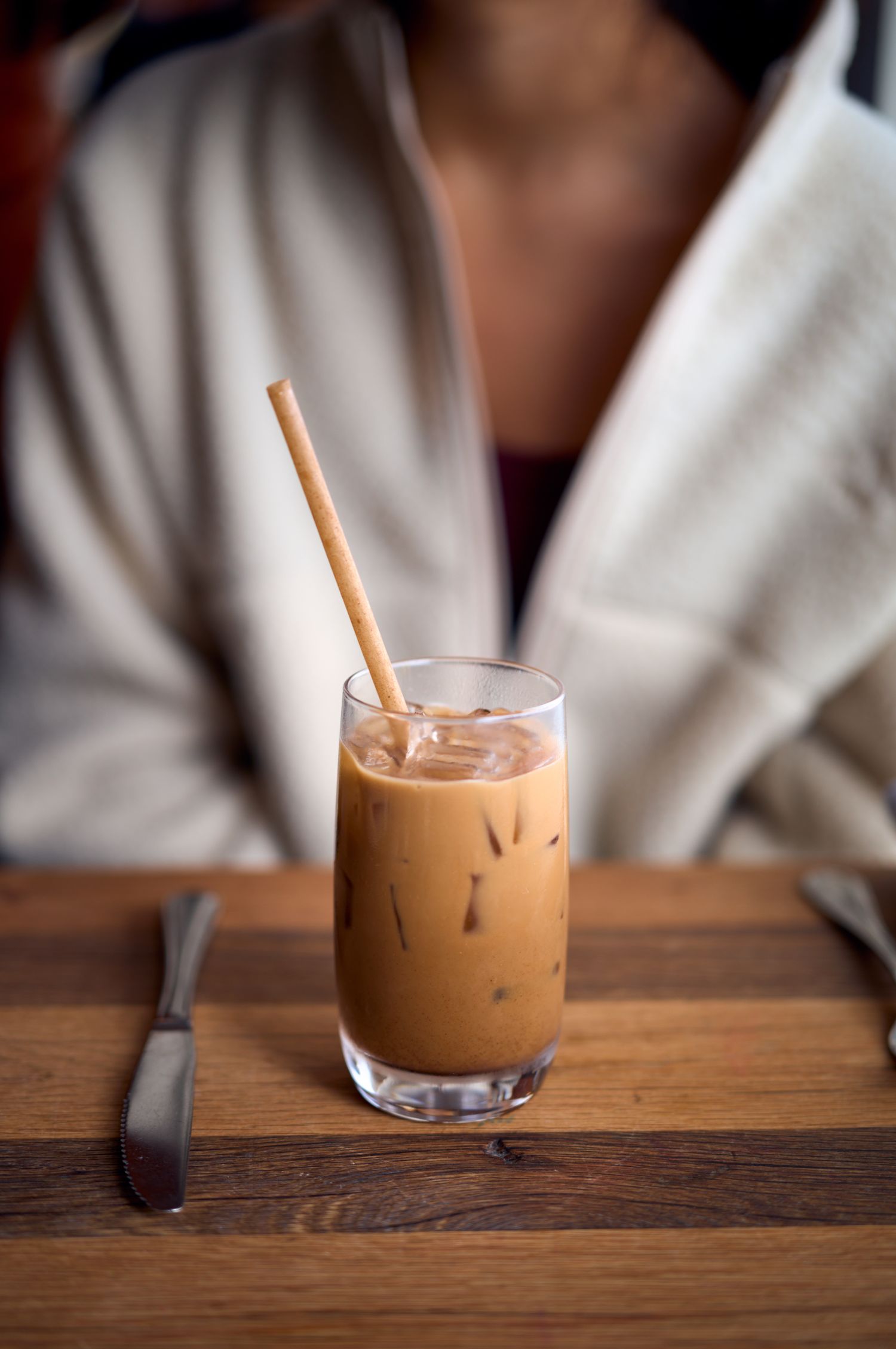 An iced coffee drink with milk served in a tall glass with a straw on a wooden table.