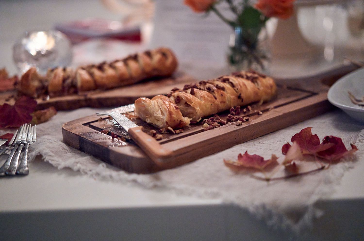 Freshly baked braided bread loaf on wooden cutting board with rose petals.
