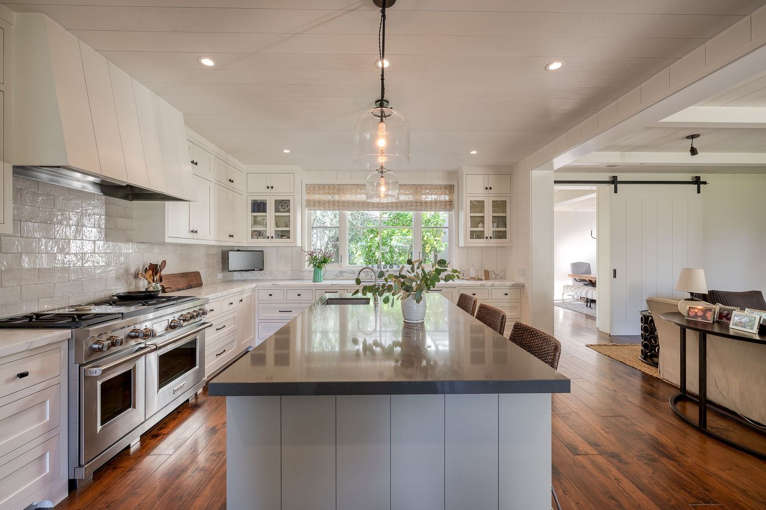 Spacious kitchen with white cabinetry, dark countertops, professional range, and large center island.