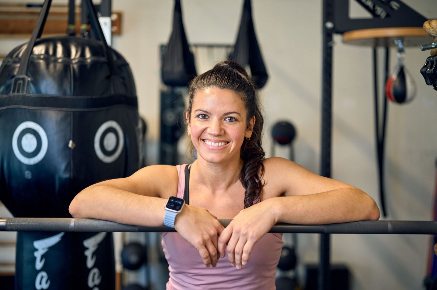 Athletic person smiling while leaning on gym equipment.