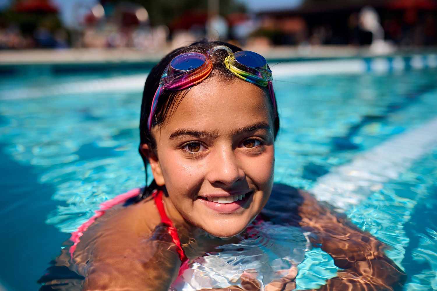 A swimmer in colorful goggles enjoys time in a bright blue swimming pool on a sunny day.