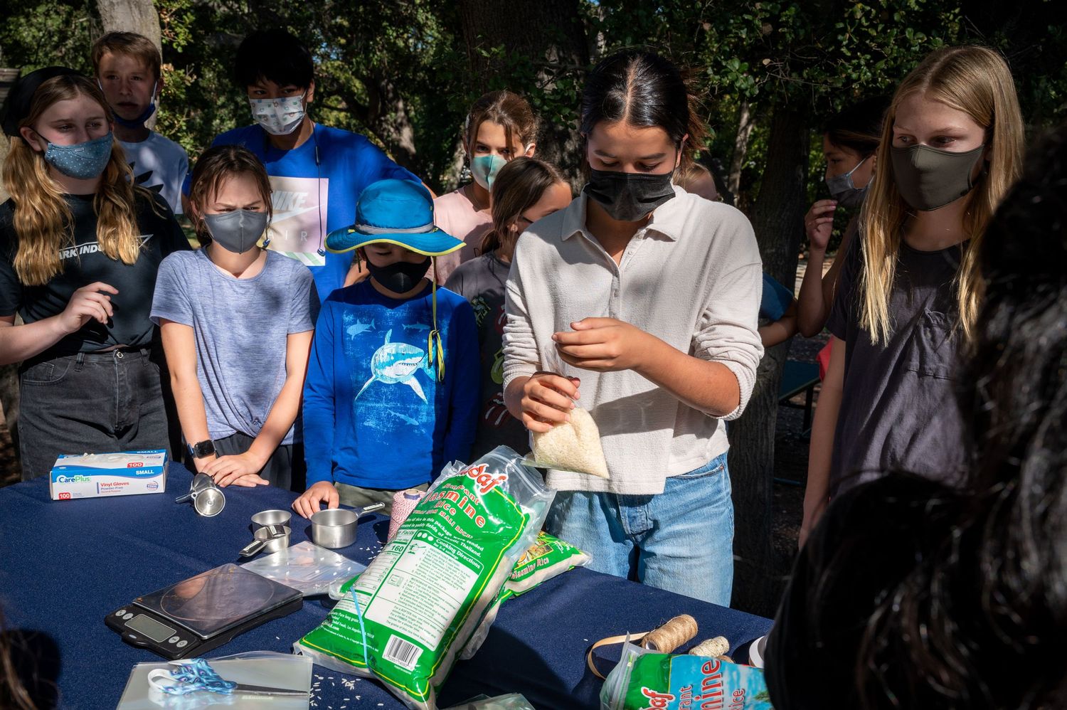 People wearing masks gather around a table with supplies outdoors.
