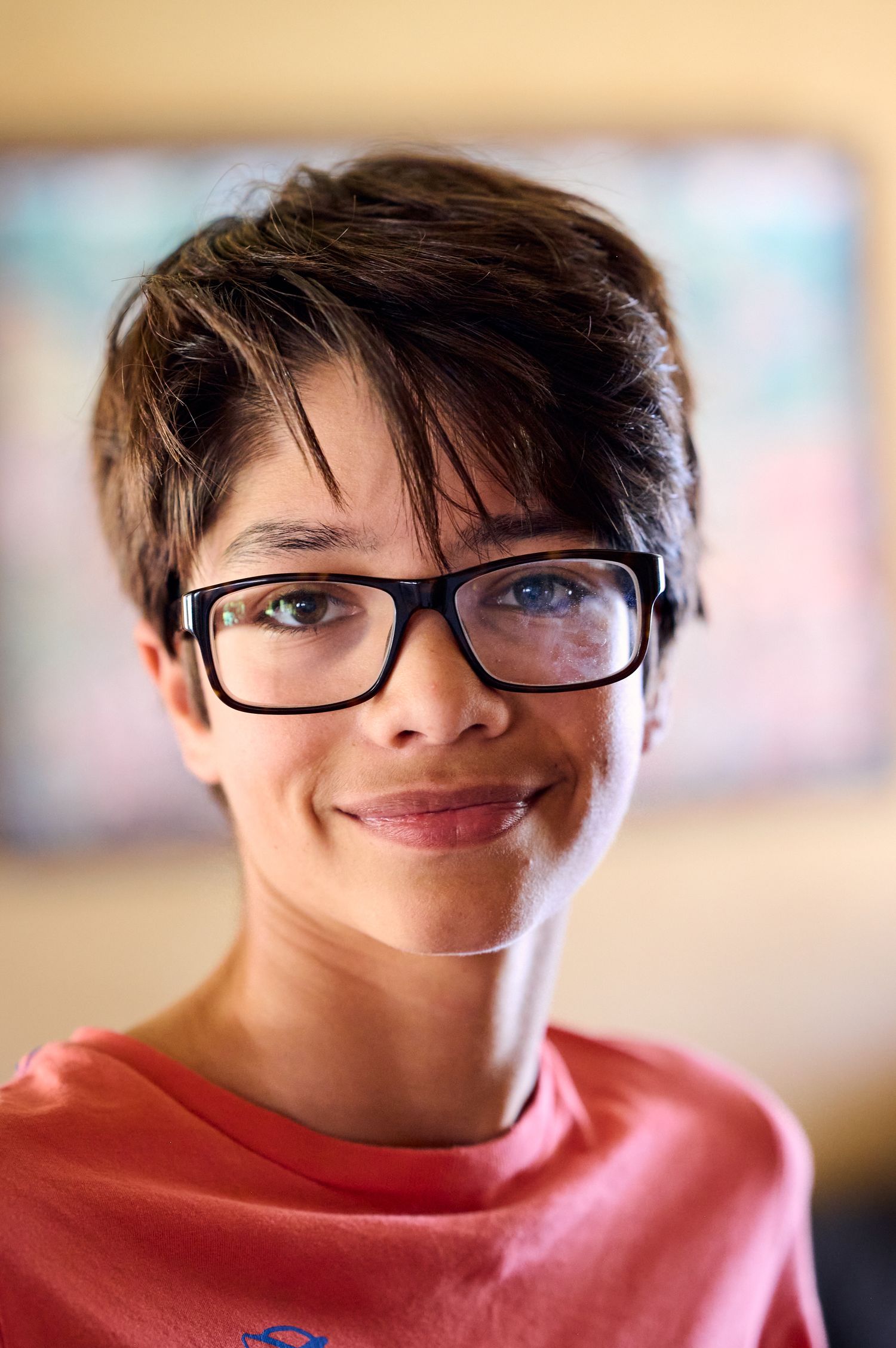 Person wearing glasses and coral colored shirt smiles warmly at camera.