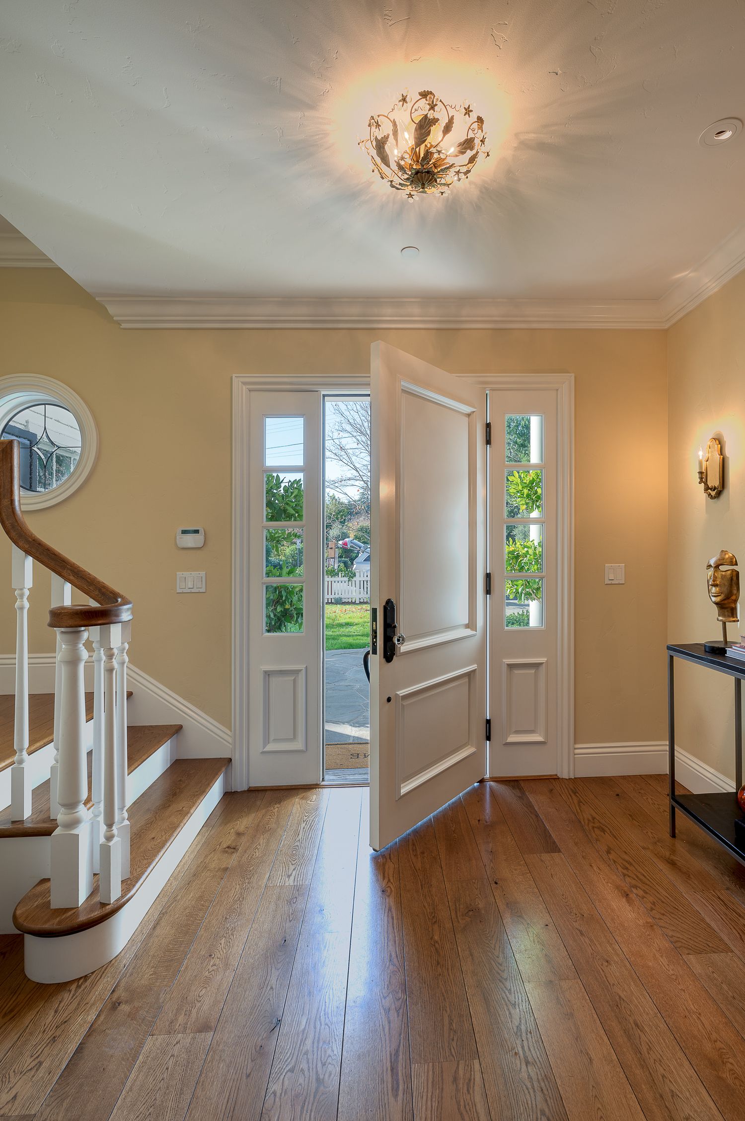 Elegant entryway with hardwood floors, white staircase, and crystal chandelier featuring French doors with glass panels.