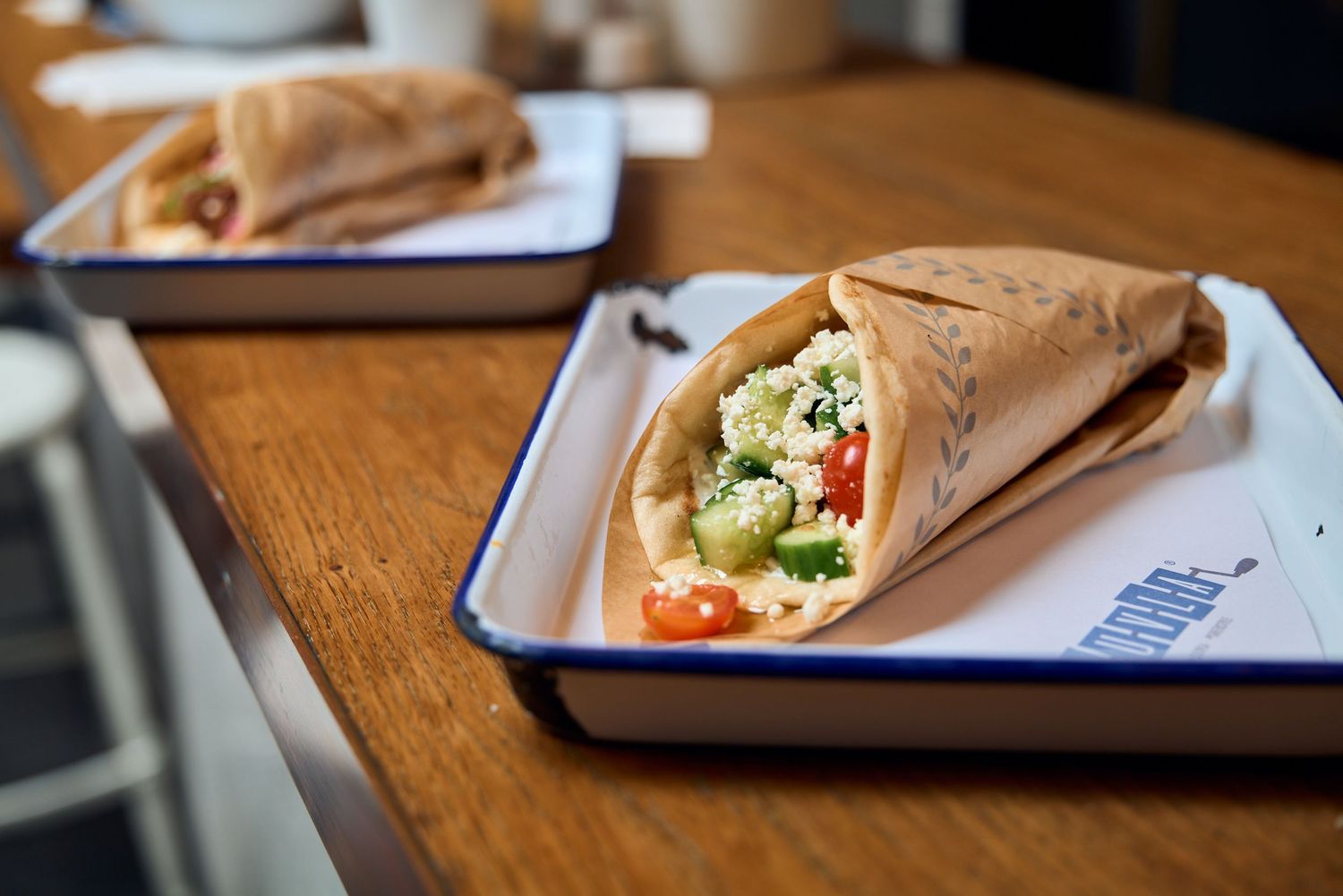 Greek-style wrap sandwich filled with vegetables and meat served on metal tray.