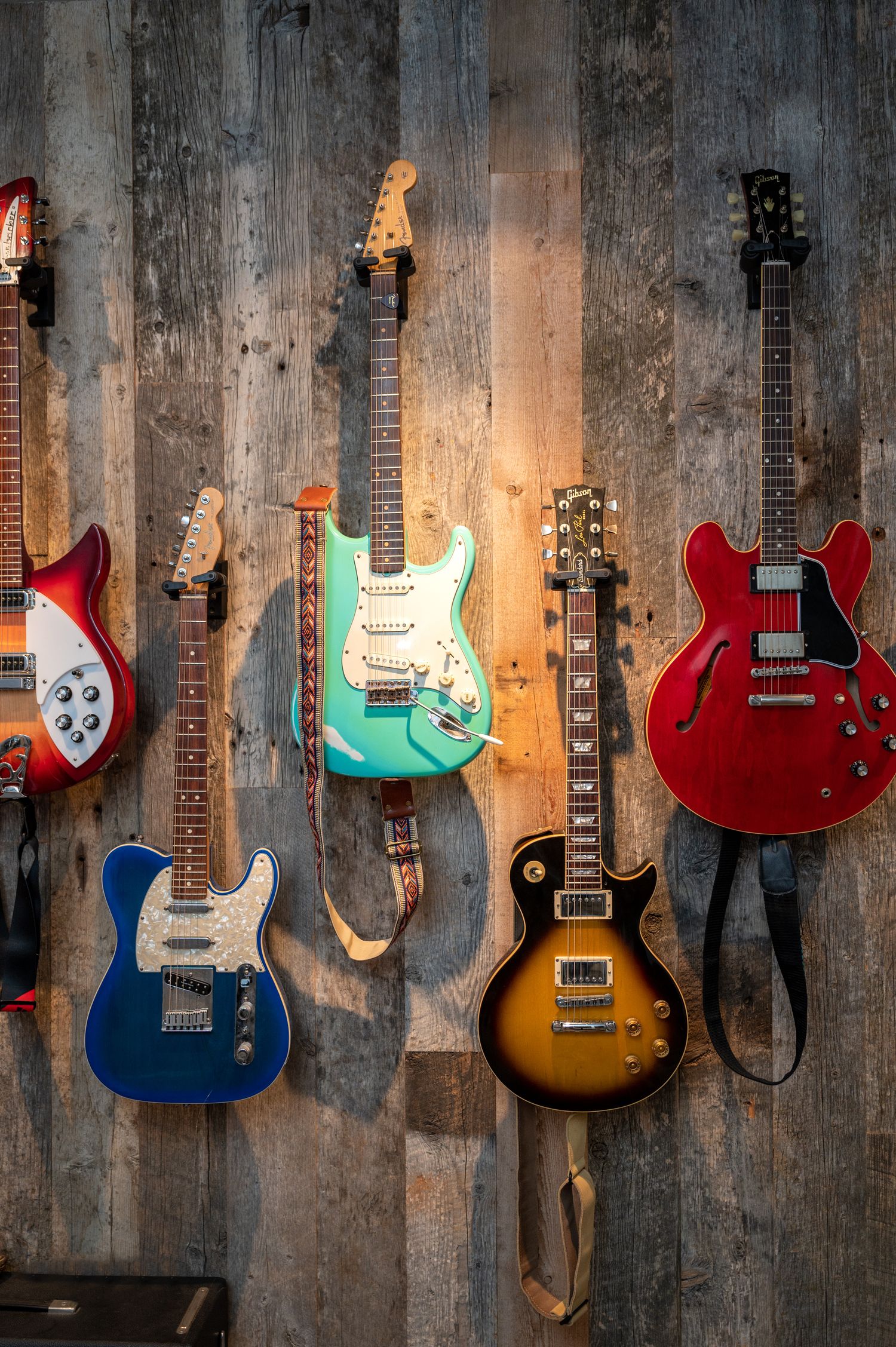 Collection of vintage electric guitars displayed on rustic wooden wall with dramatic lighting.