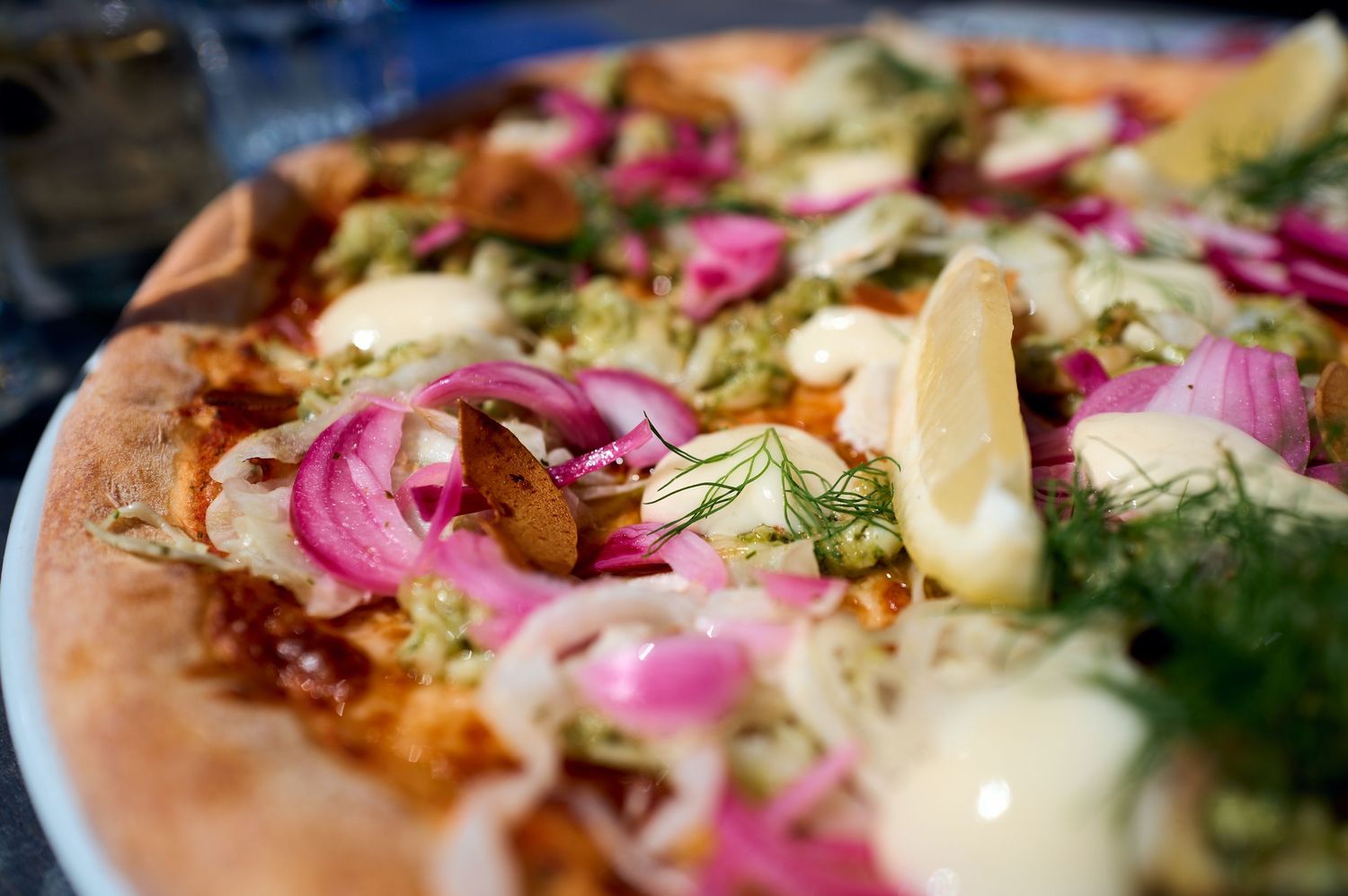 Gourmet pizza topped with red onions, fresh herbs, and lemon wedges.