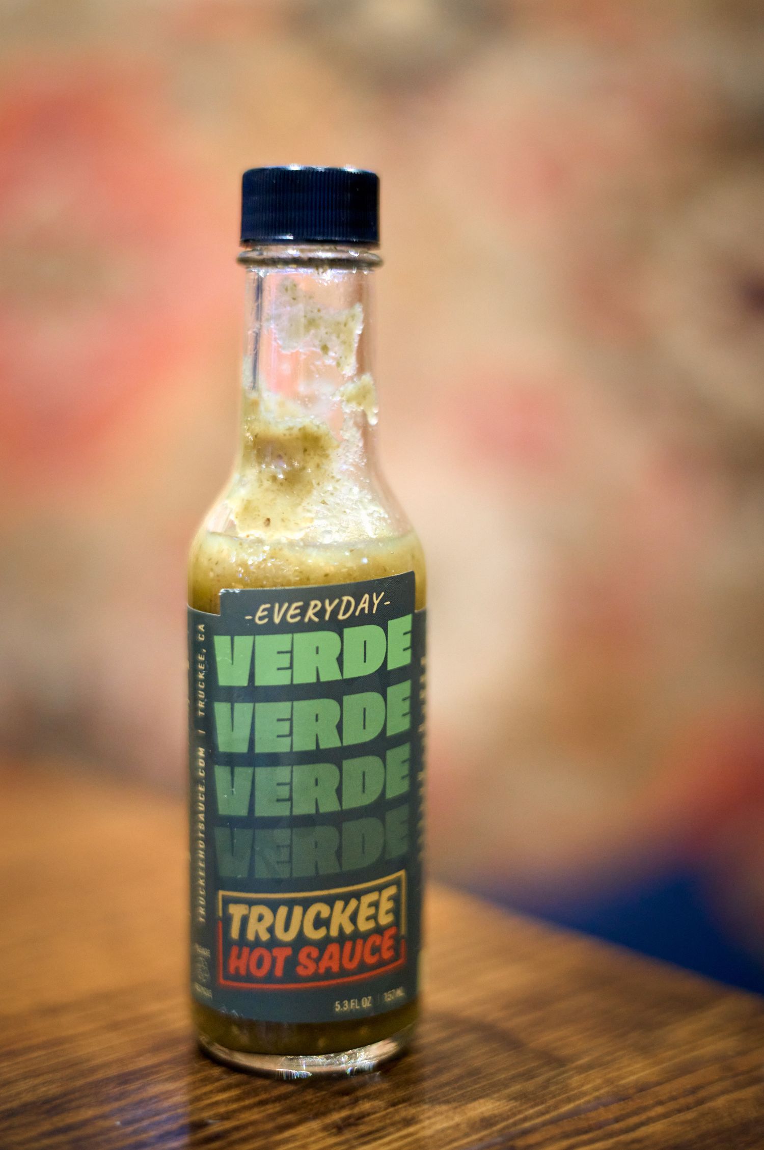 A bottle of Verde Verde Truckee hot sauce on a wooden surface with blurred background.