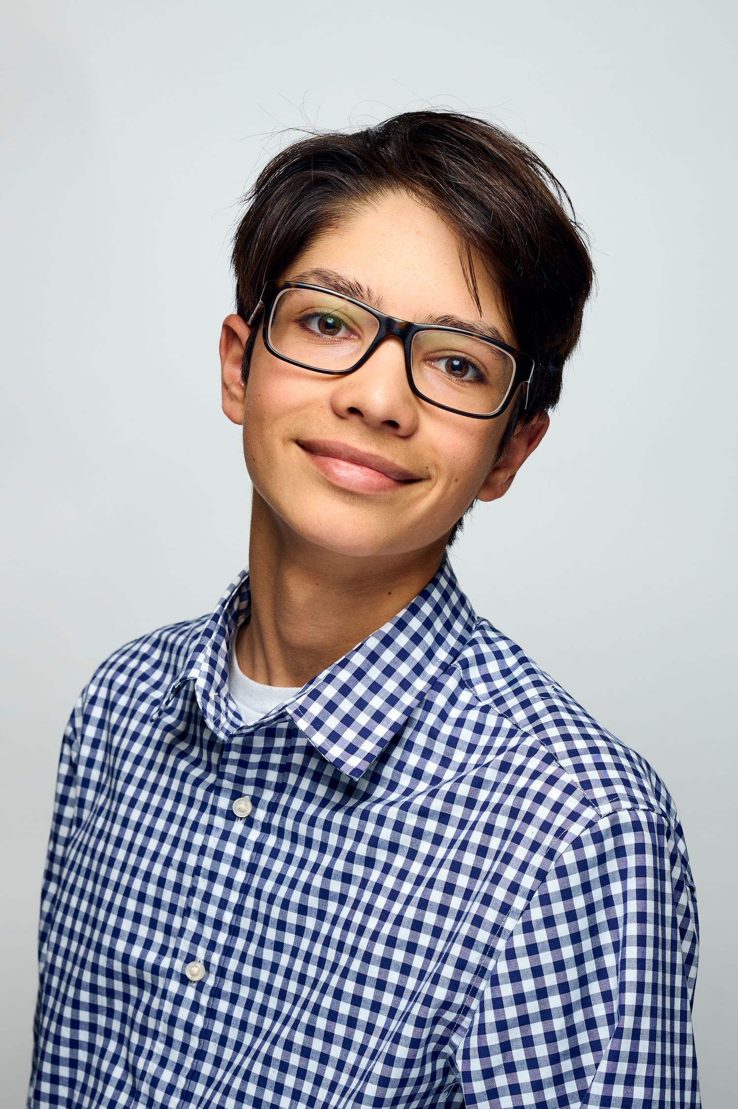 Person wearing glasses and a blue gingham check shirt smiles warmly against a light background.