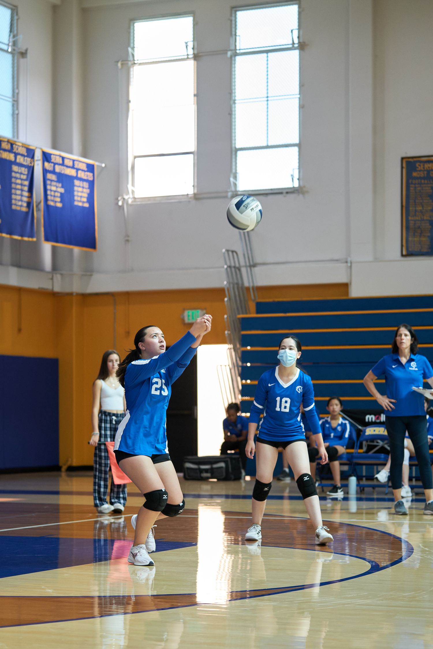 Volleyball player in blue uniform serving the ball during indoor game.