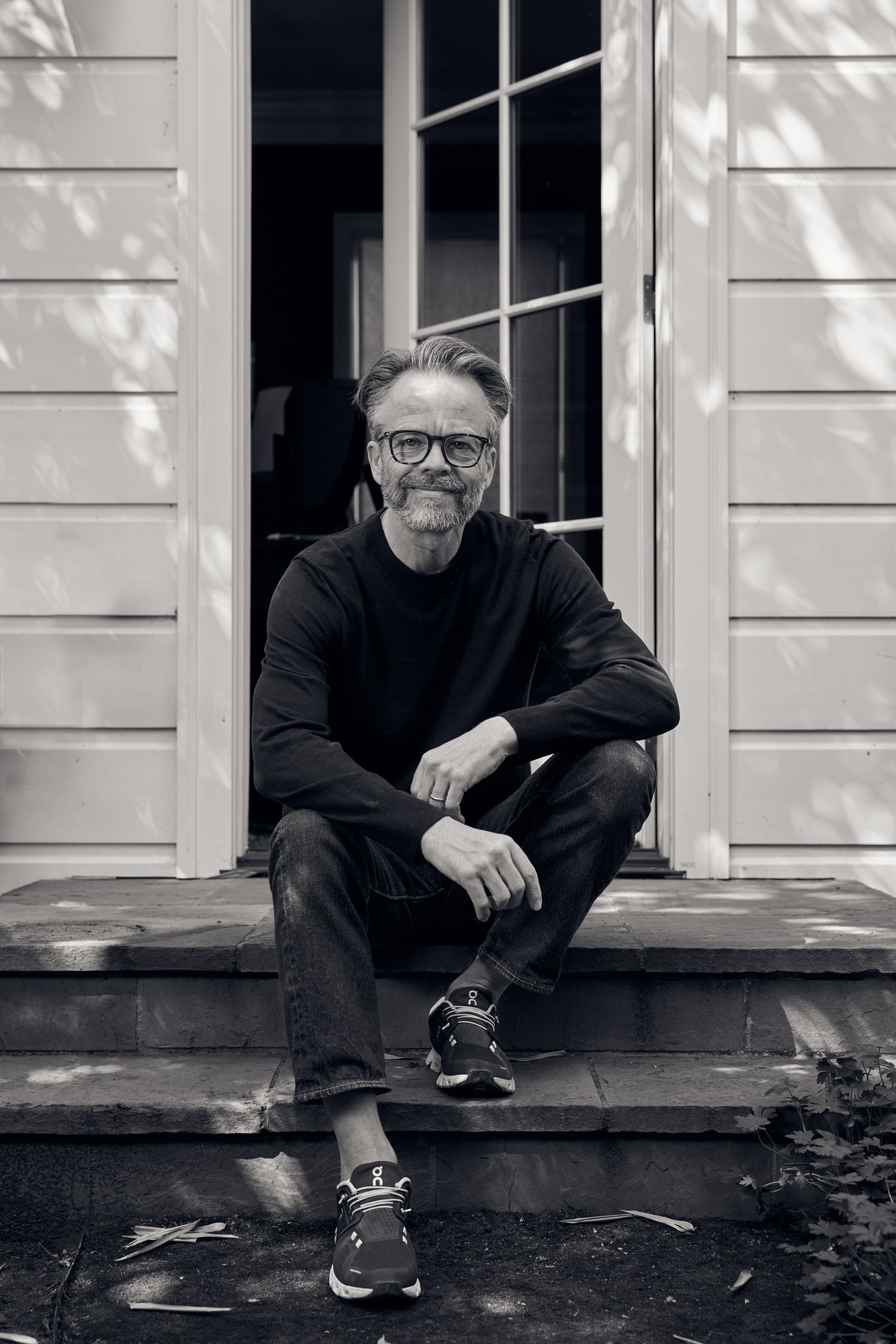 A black and white portrait of someone sitting on wooden steps wearing glasses and casual attire.
