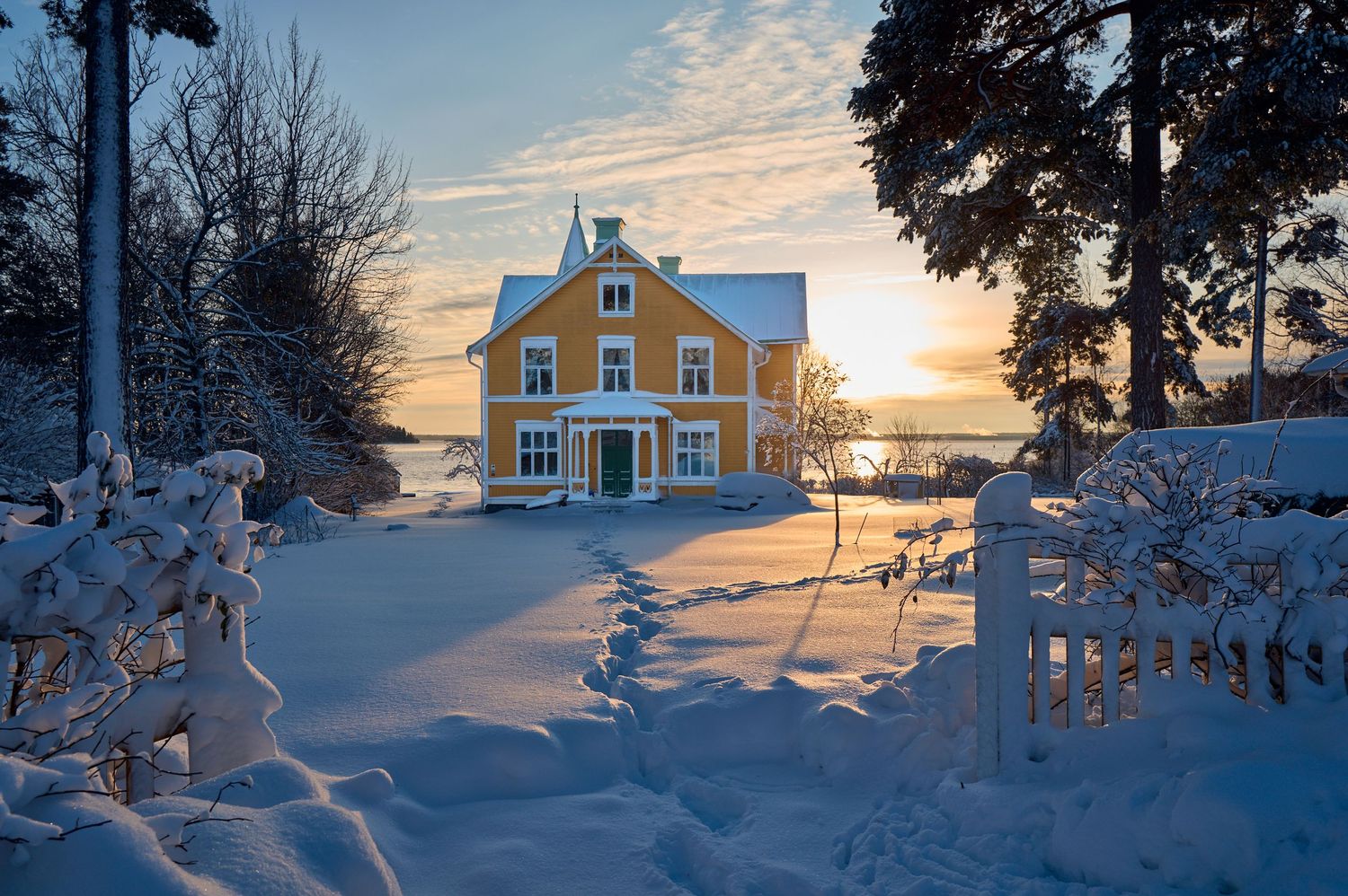 Yellow house covered in snow at sunset with dramatic winter sky.