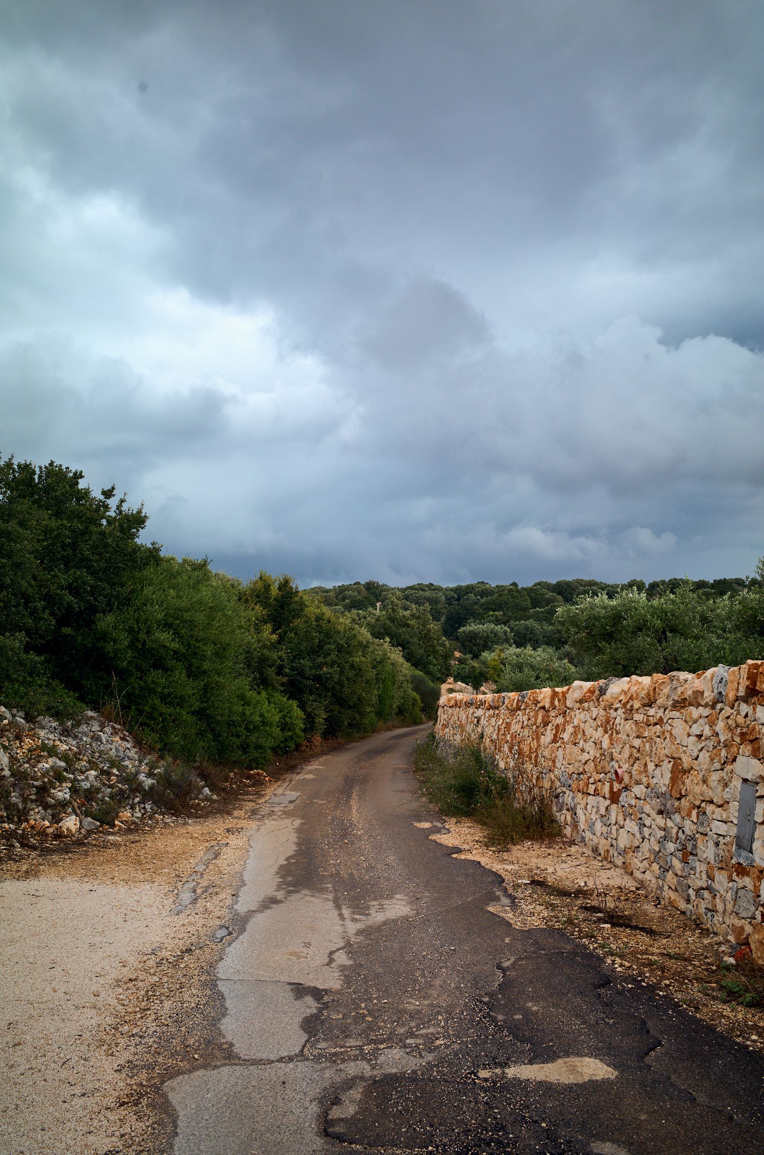 Stone wall lines a winding country road under stormy grey clouds.