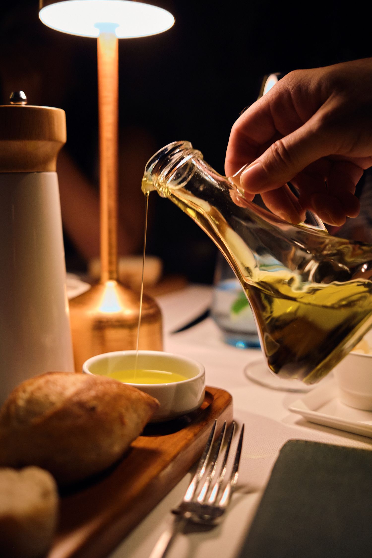 Pouring golden olive oil into a small dish at an elegant dinner table setting.