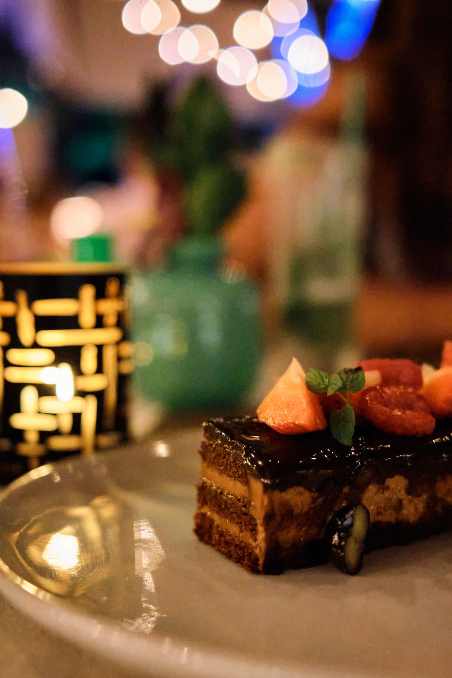 Chocolate layered cake slice garnished with fresh fruit and served in ambient lighting.