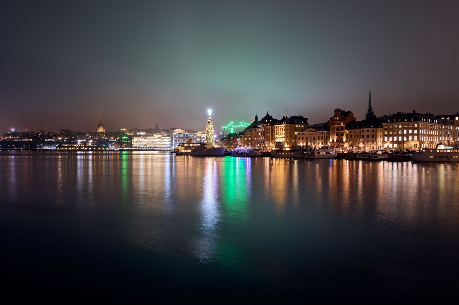 City skyline illuminated at night with colorful lights reflecting on peaceful waterfront.