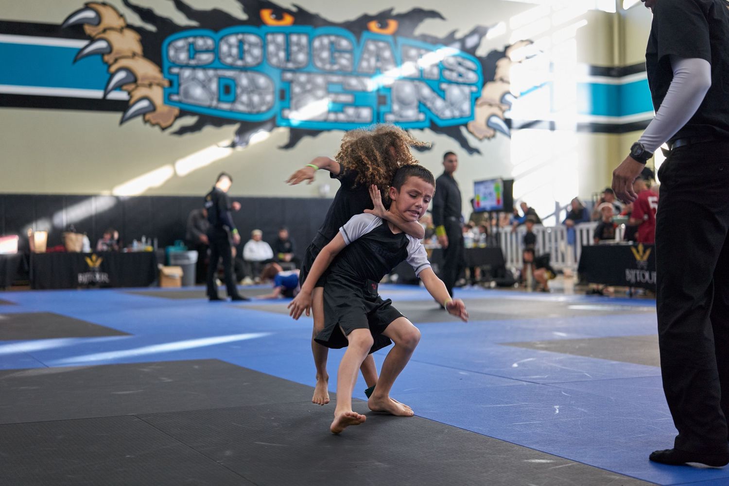 A young athlete performs a martial arts move on blue mats during a competition.