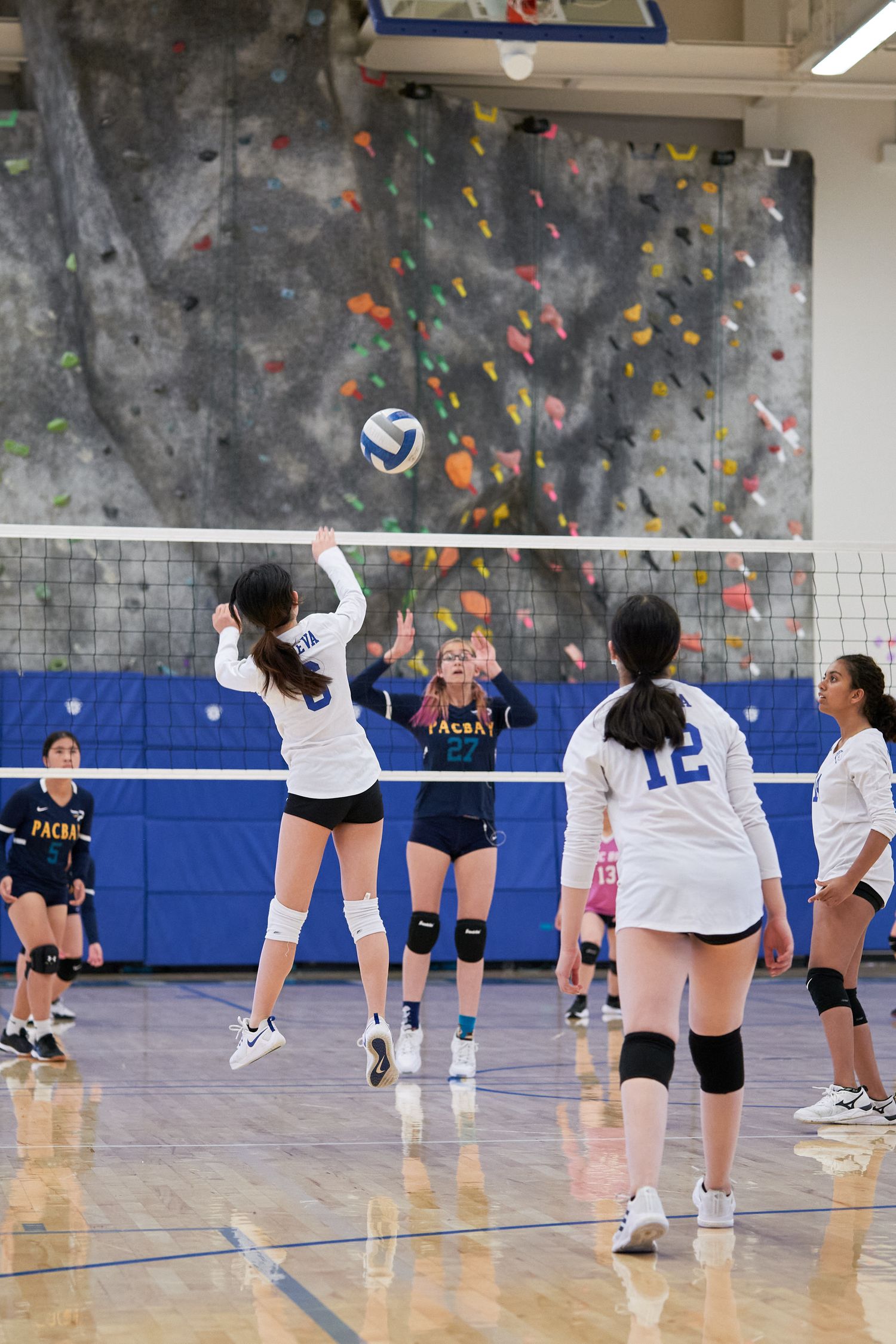 Player leaping at net for volleyball spike with climbing wall visible in background.